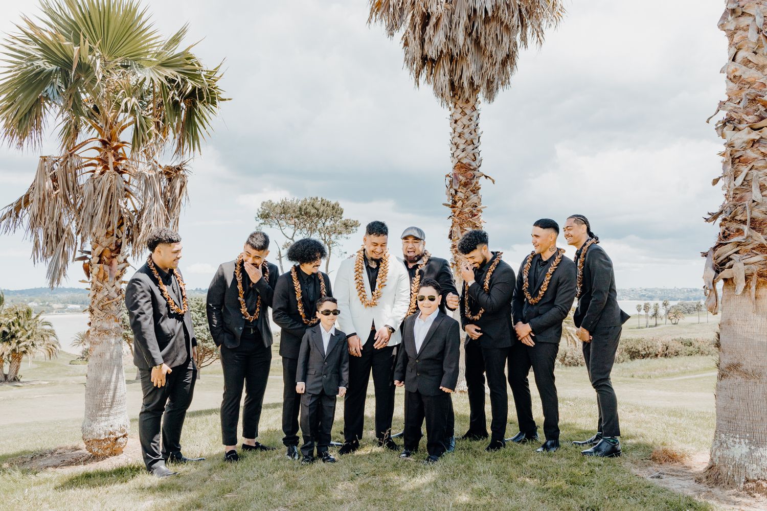 Wedding party in black and white attire poses together under tropical palm trees.