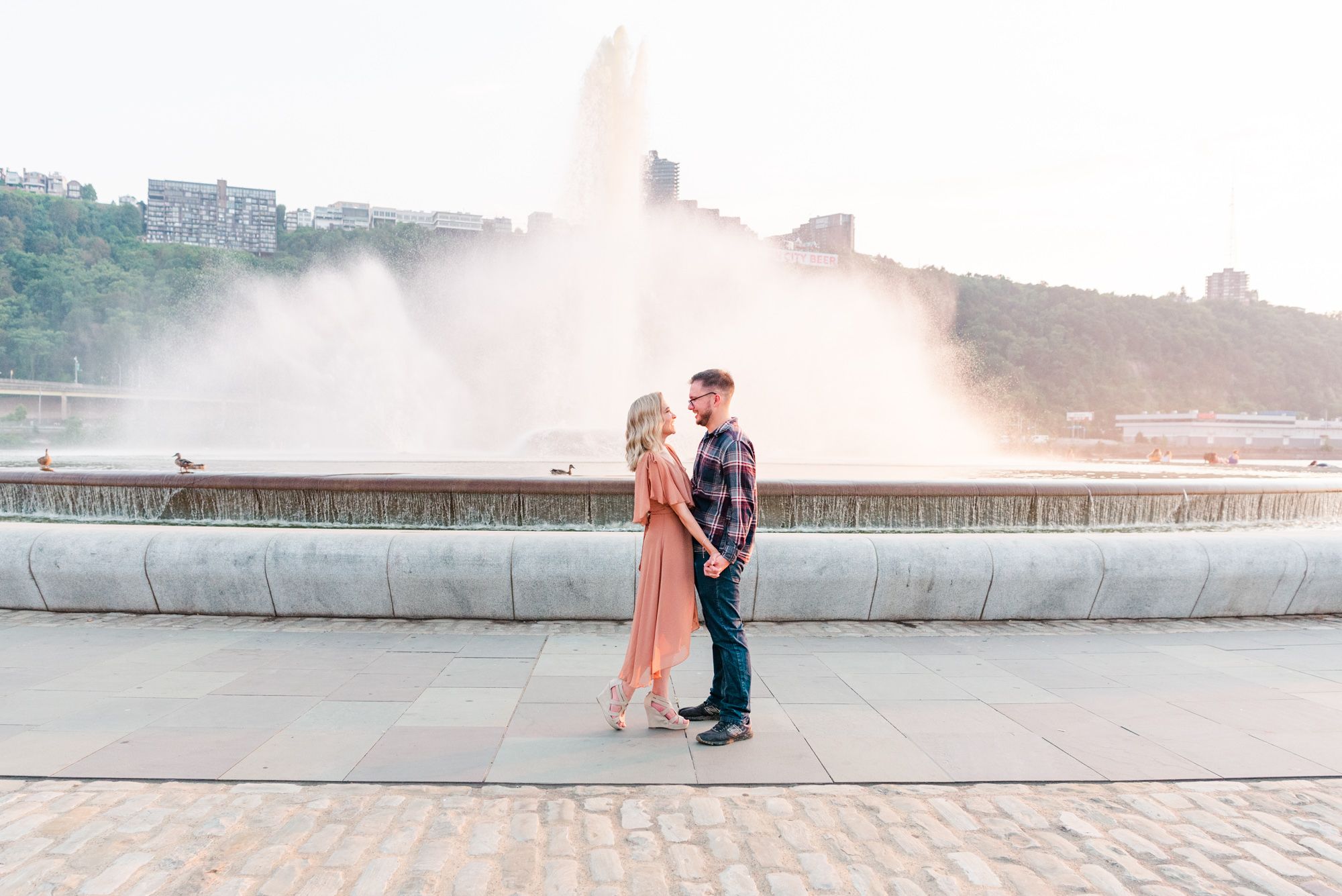 Surprise proposal at sunset with couple standing in front of fountain at Point State Park in Pittsburgh, Pennsylvania