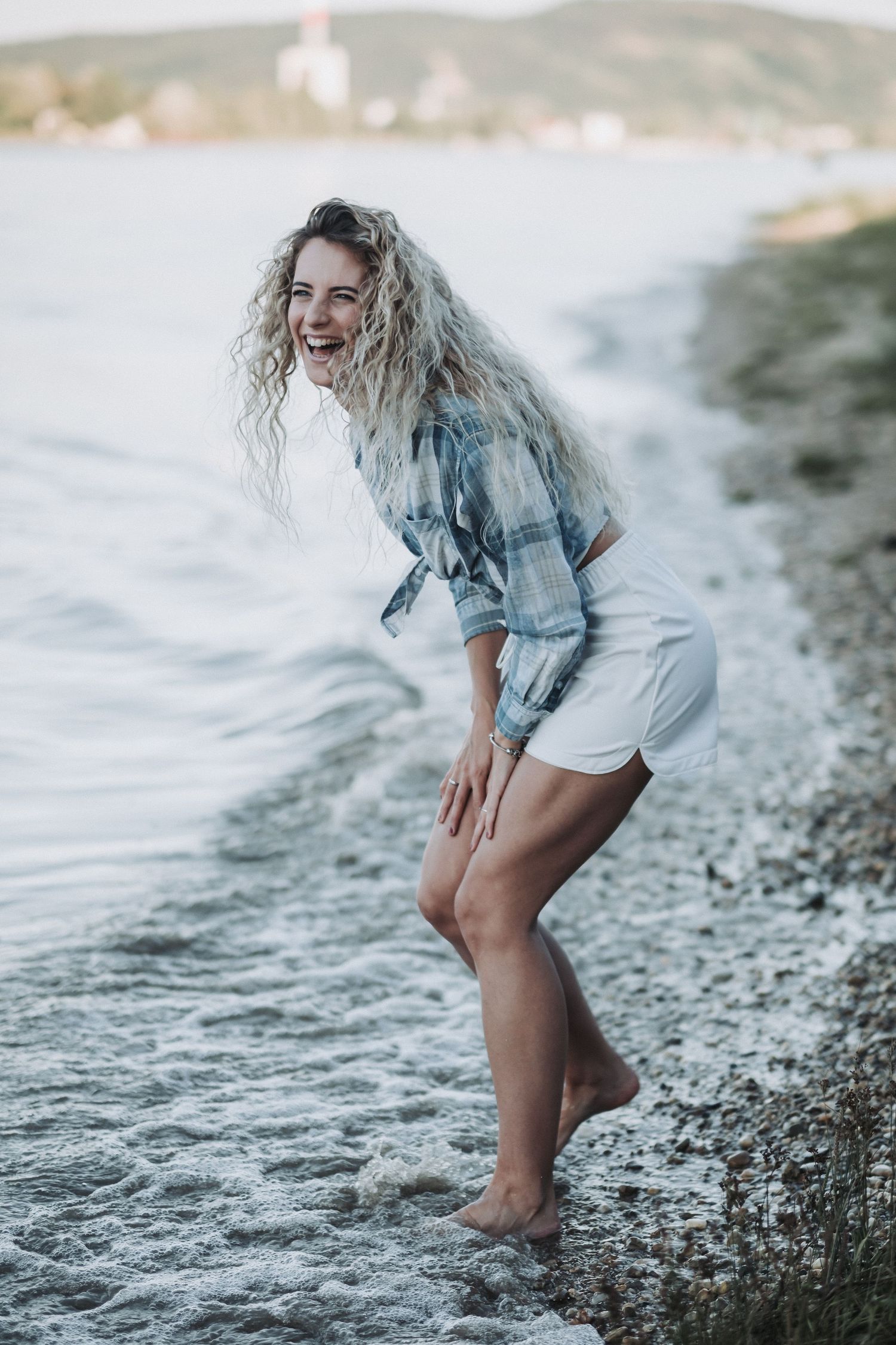 Person in plaid shirt and shorts laughing while playing in ocean water.