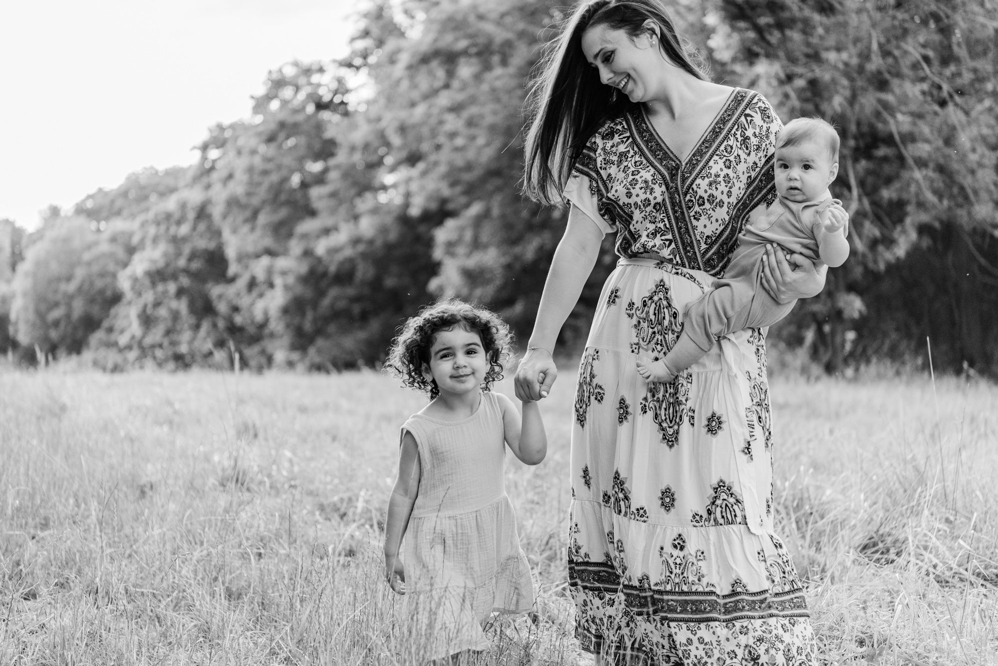 Mom and young daughters walking through field in black and white in Pittsburgh, Pennsylvania