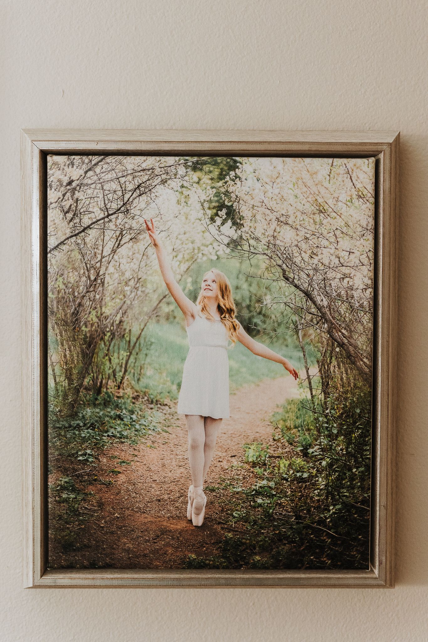 A framed photograph of a ballet dancer in a white dress gracefully posing on pointe among blooming spring branches.