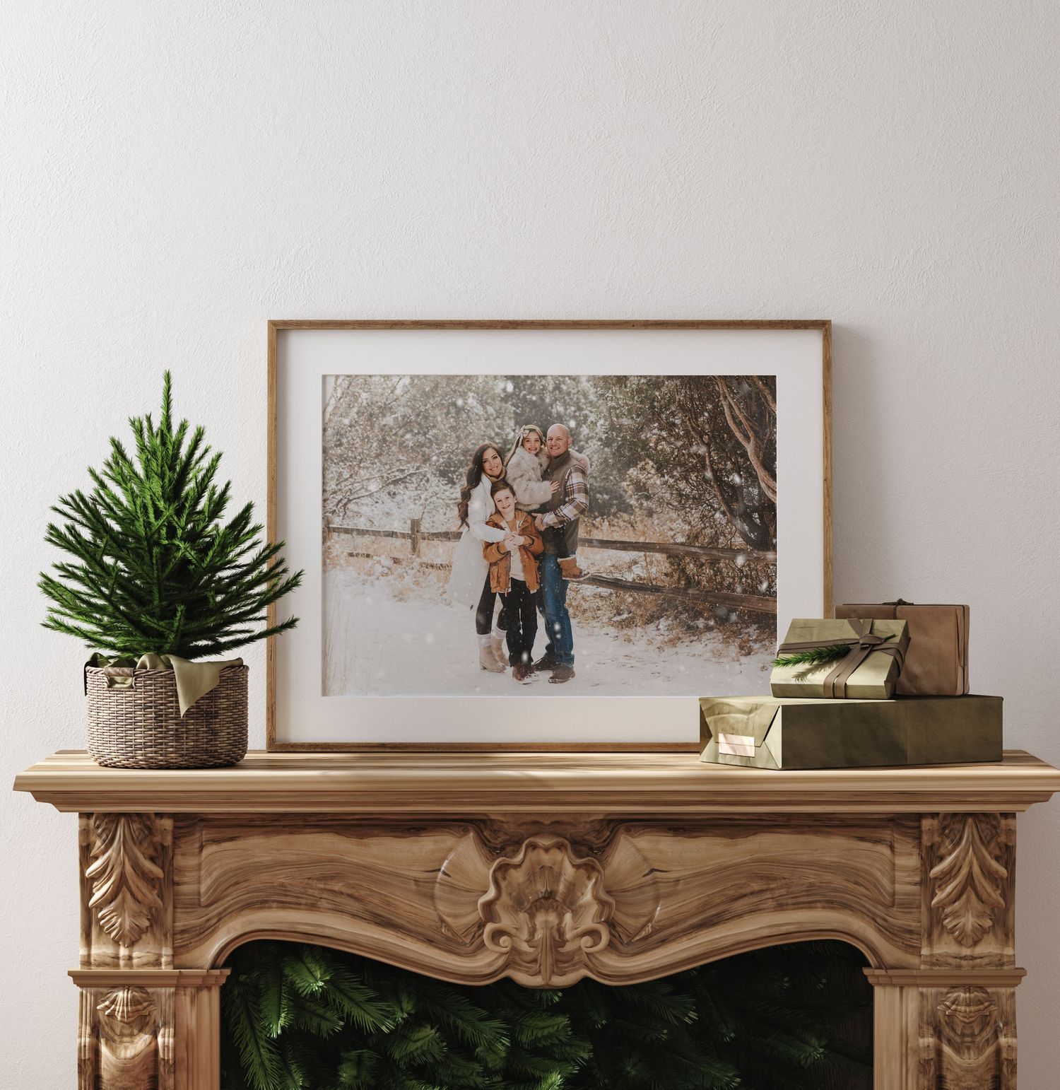 A framed winter photograph sits on an ornate wooden mantel with a small evergreen tree and decorative box beside it.