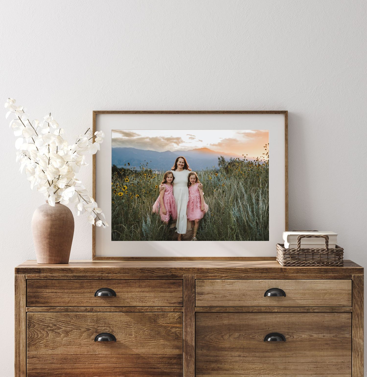 Framed outdoor photograph displayed on wood dresser with white florals in ceramic vase and decorative box.