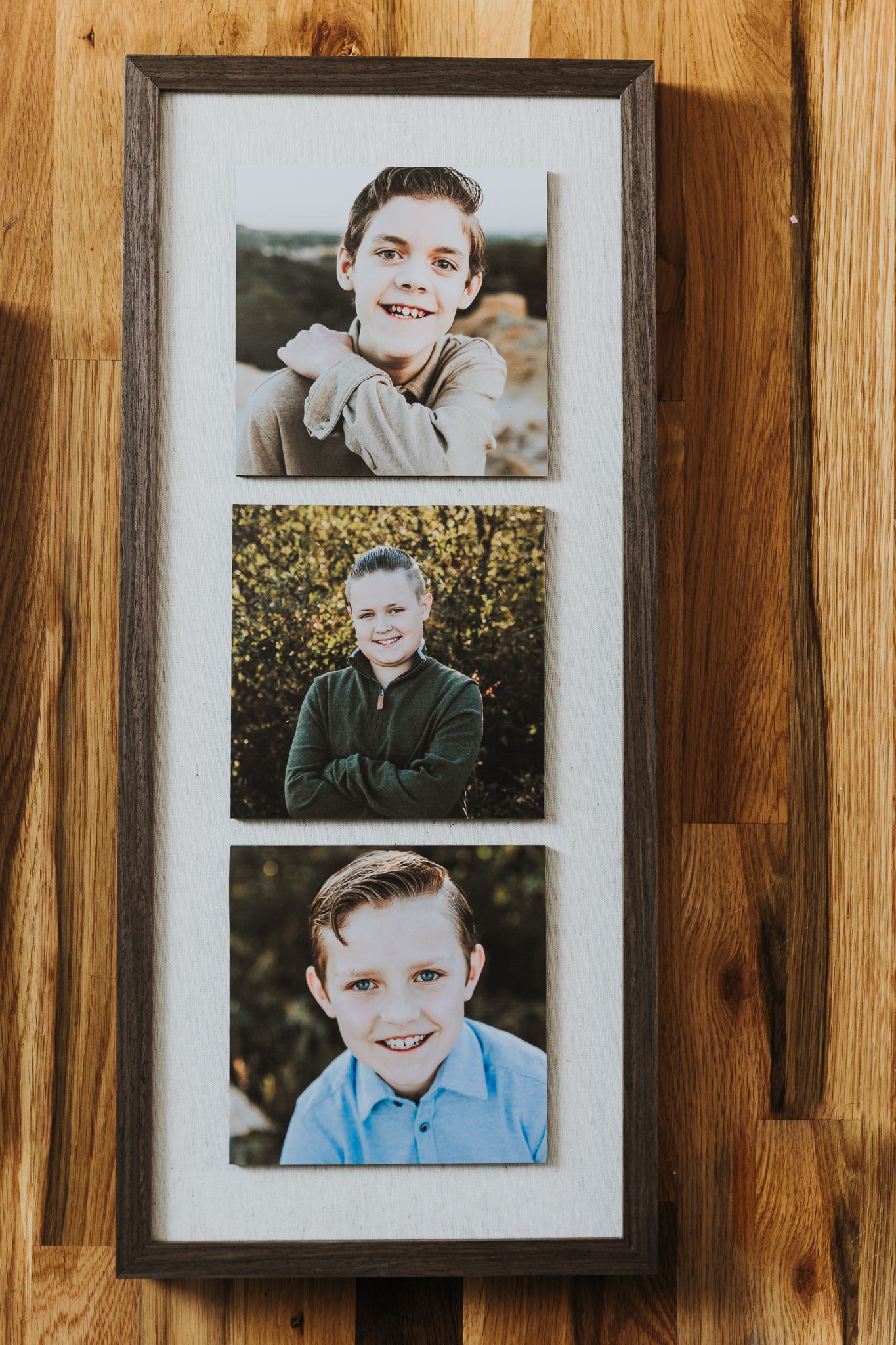 A vertical framed portrait collage with three photos arranged in a brown wooden frame hanging on a wood plank wall.