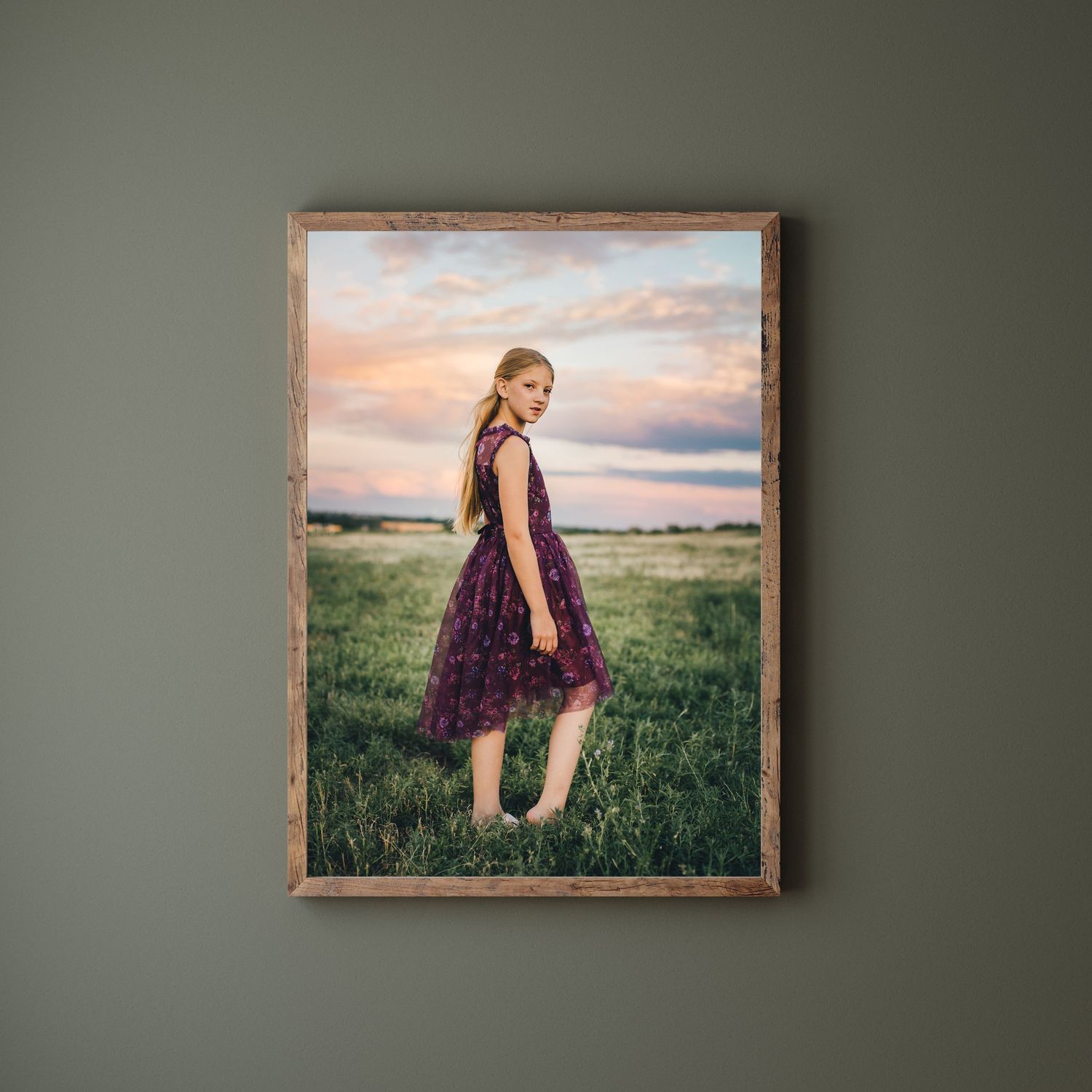 Framed photograph on gray wall showing a rural setting at sunset with figure in purple dress standing in grassy field.