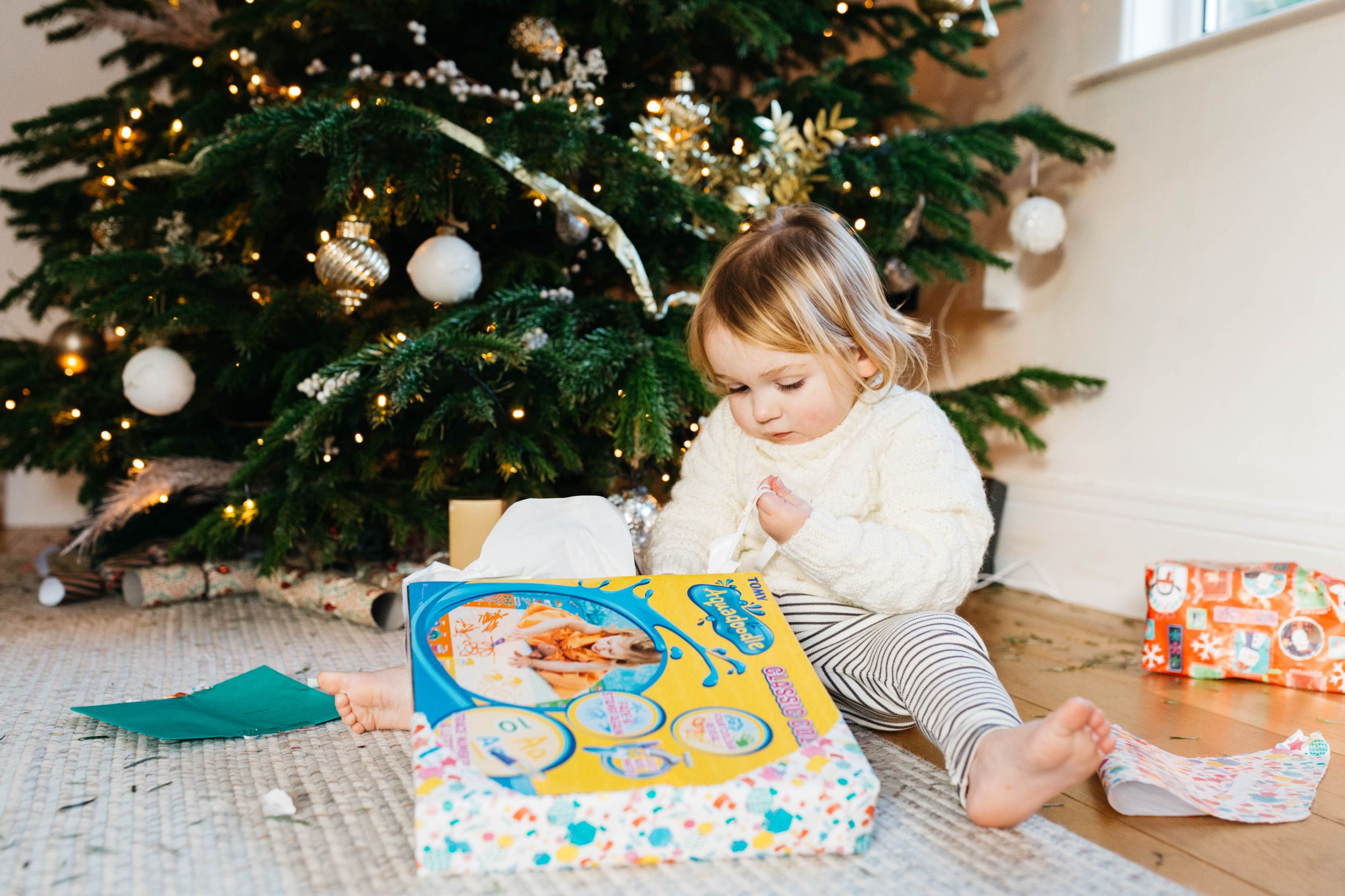 toddler boy in white jumper opening up Christmas present