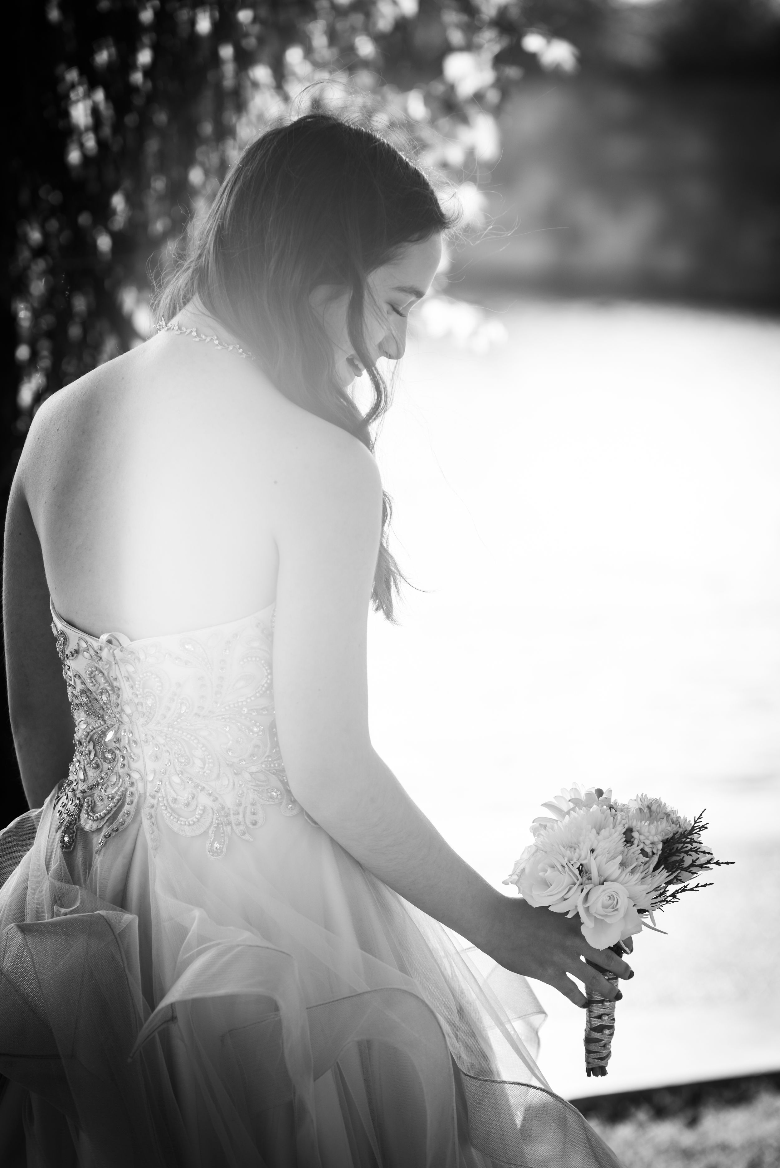 Artistic black and white photo of bride holding bouquet in dreamy backlit setting.