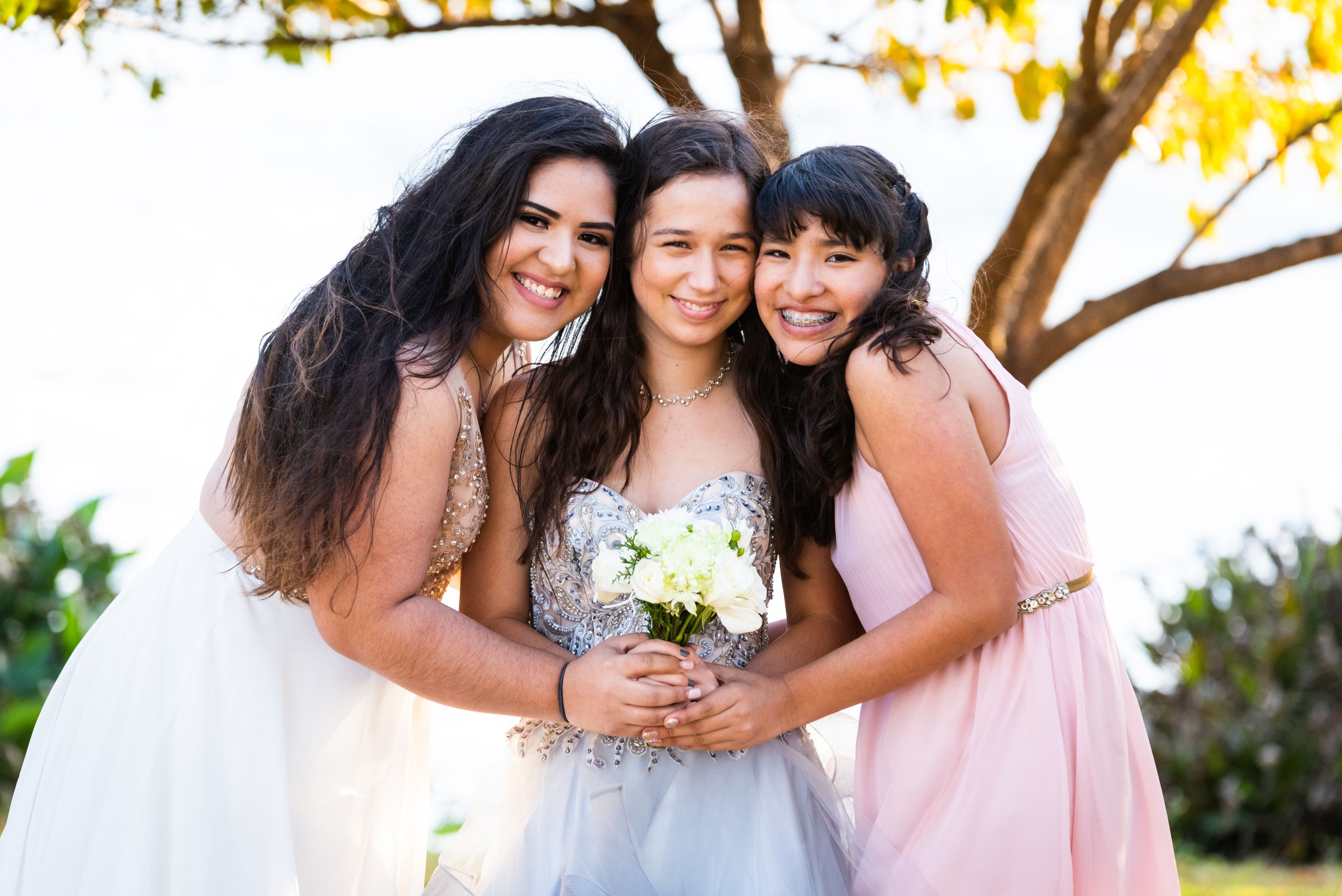 Three bridesmaids in pink and white dresses share a joyful moment together outdoors.