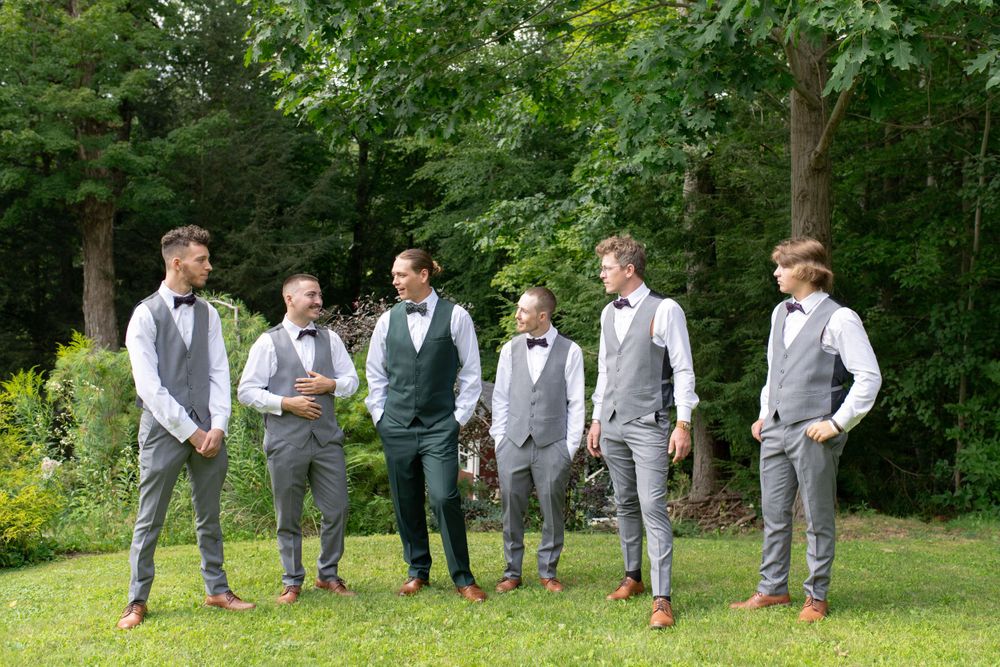 Groomsmen in matching grey vests and pants pose together outdoors in a garden setting.