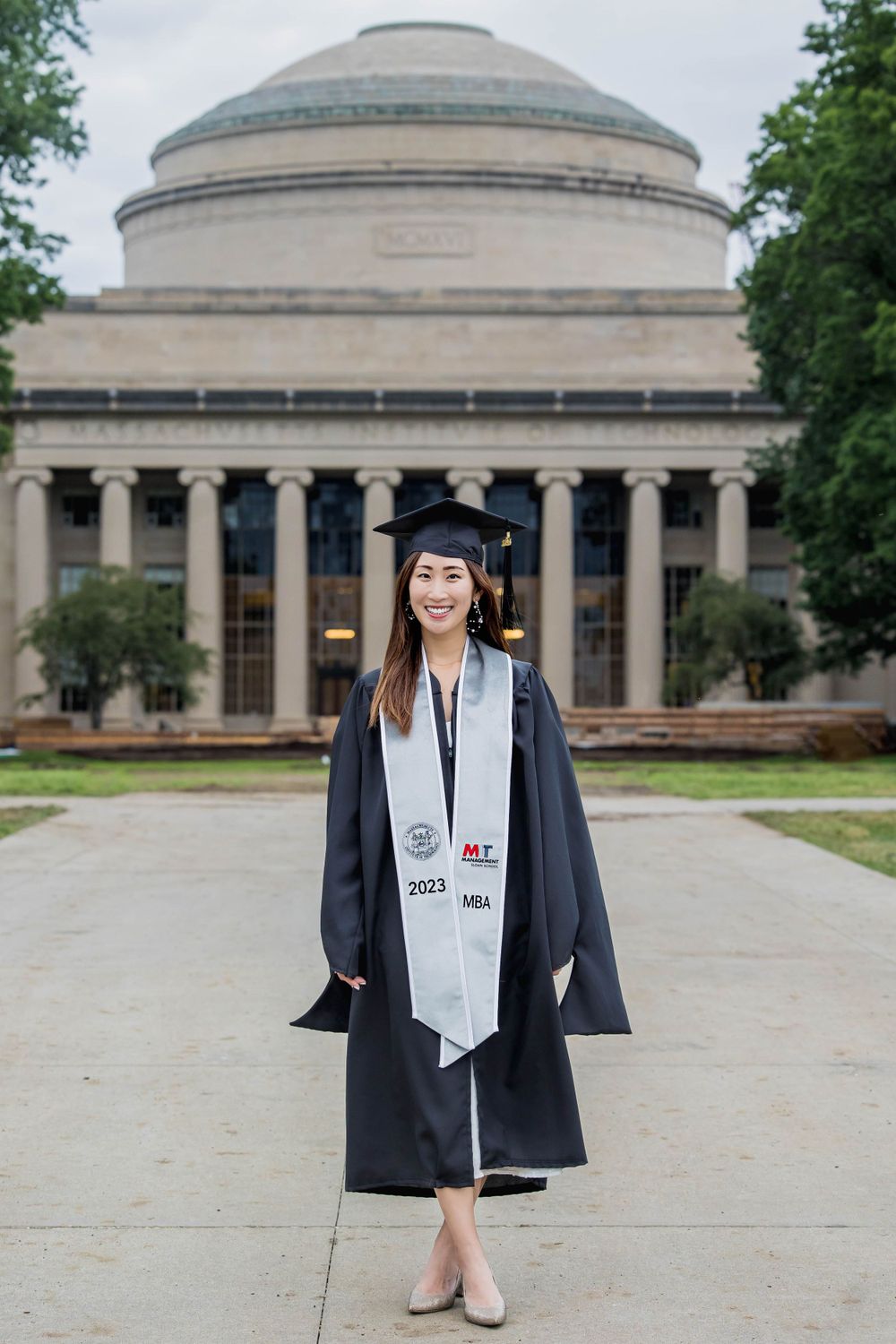 Graduate posing in cap and gown in front of MIT's iconic Great Dome building.