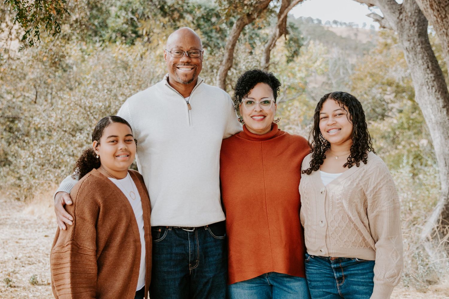 Family of four wearing cozy sweaters pose together for an outdoor autumn portrait.
