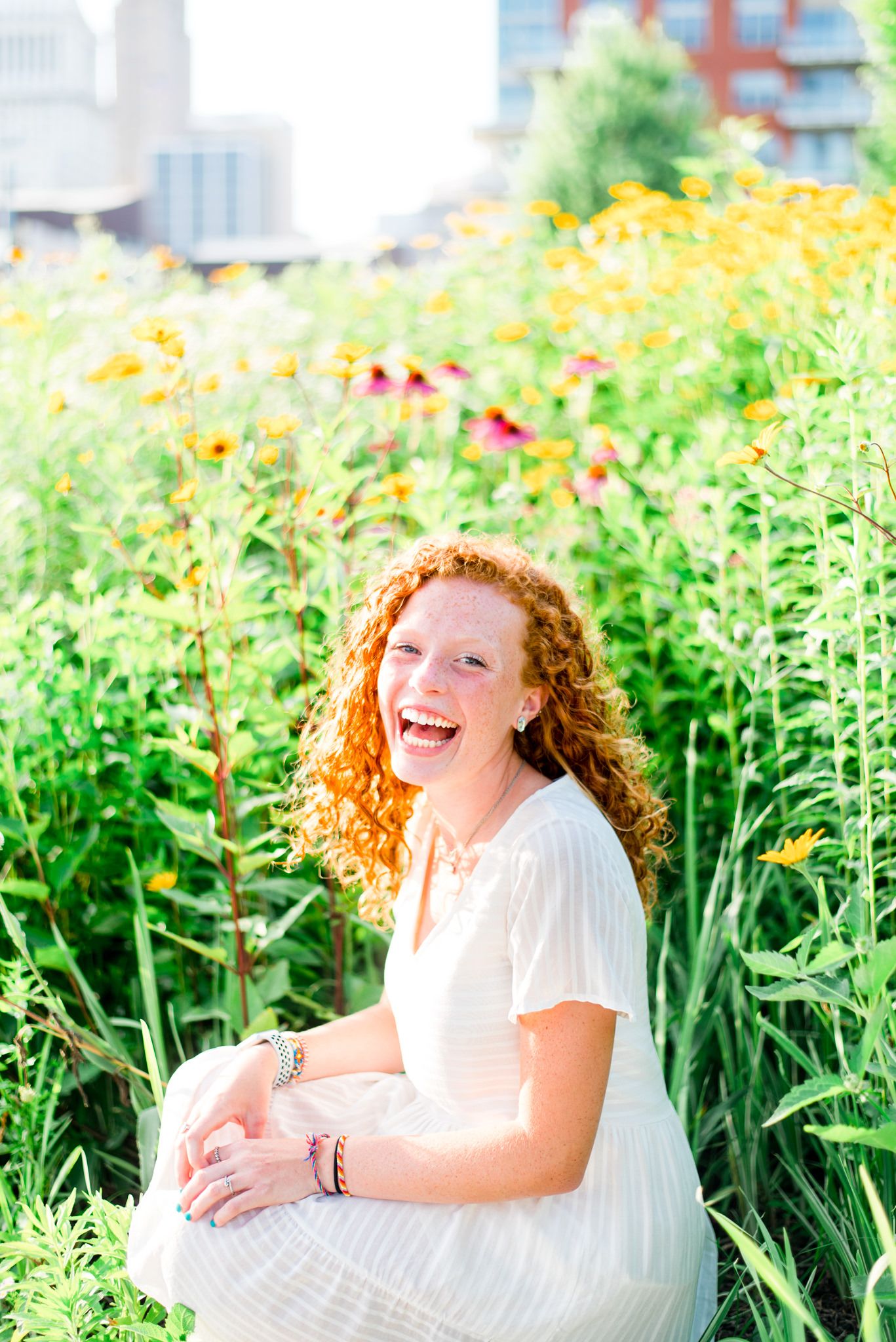 young woman with curly red hair laughing widely in the yellow and pink flowers at Smale Park at sunset