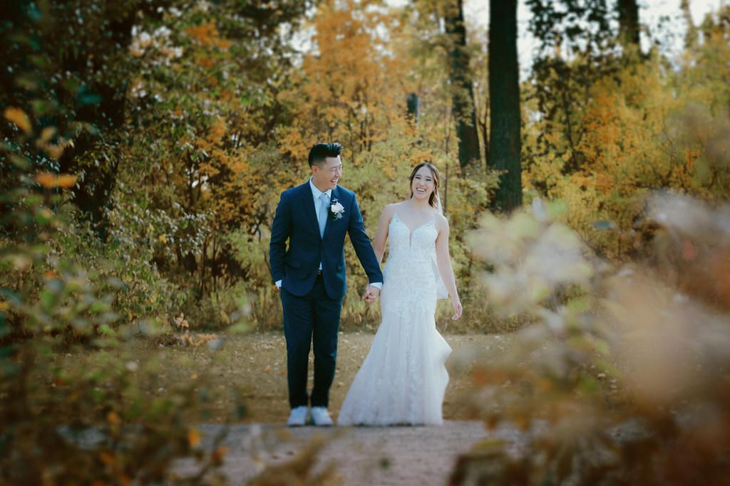 A couple walks along an autumn path surrounded by golden foliage and trees.