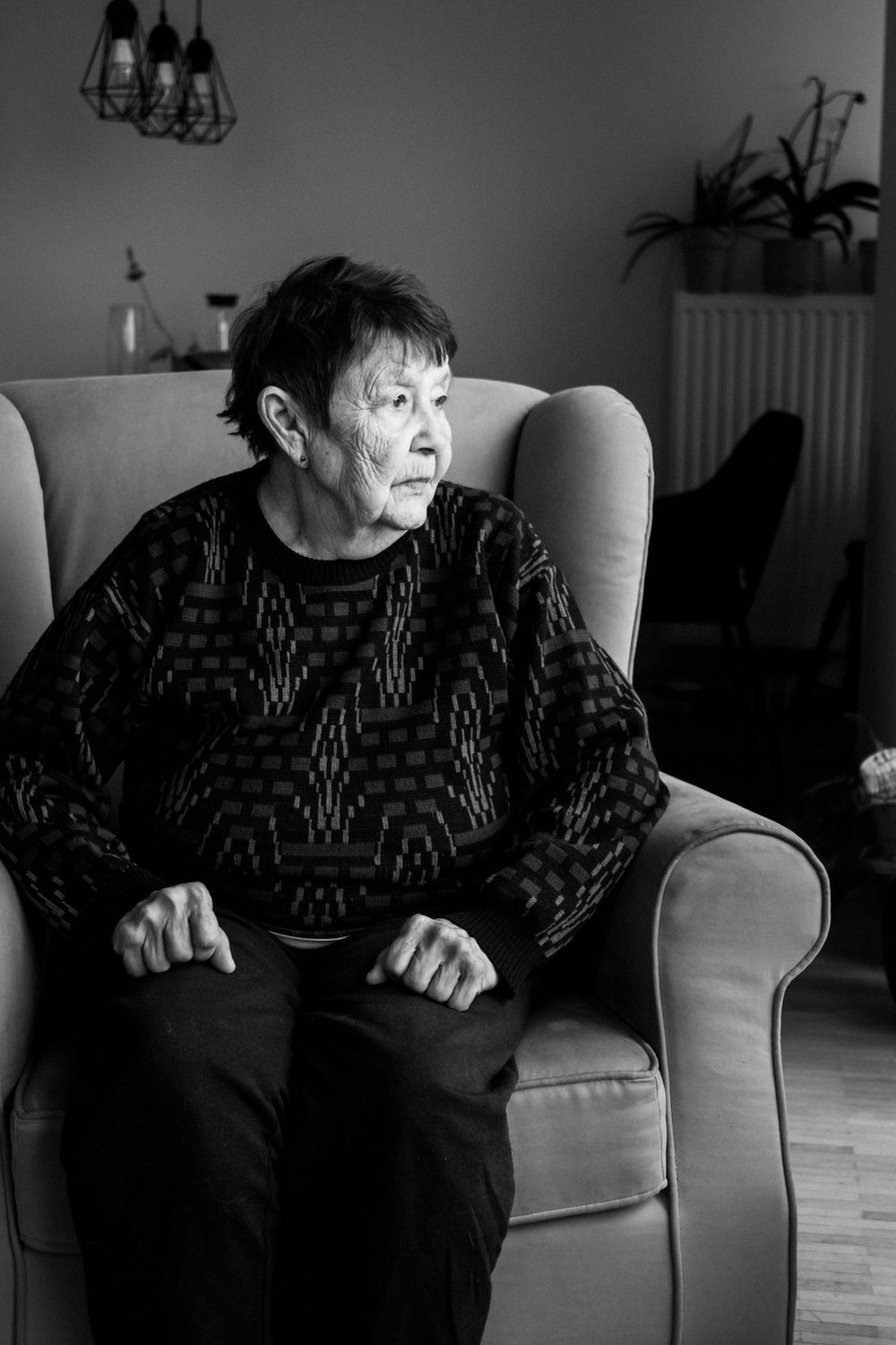 Elderly person in a patterned sweater sitting in an armchair, shot in black and white.