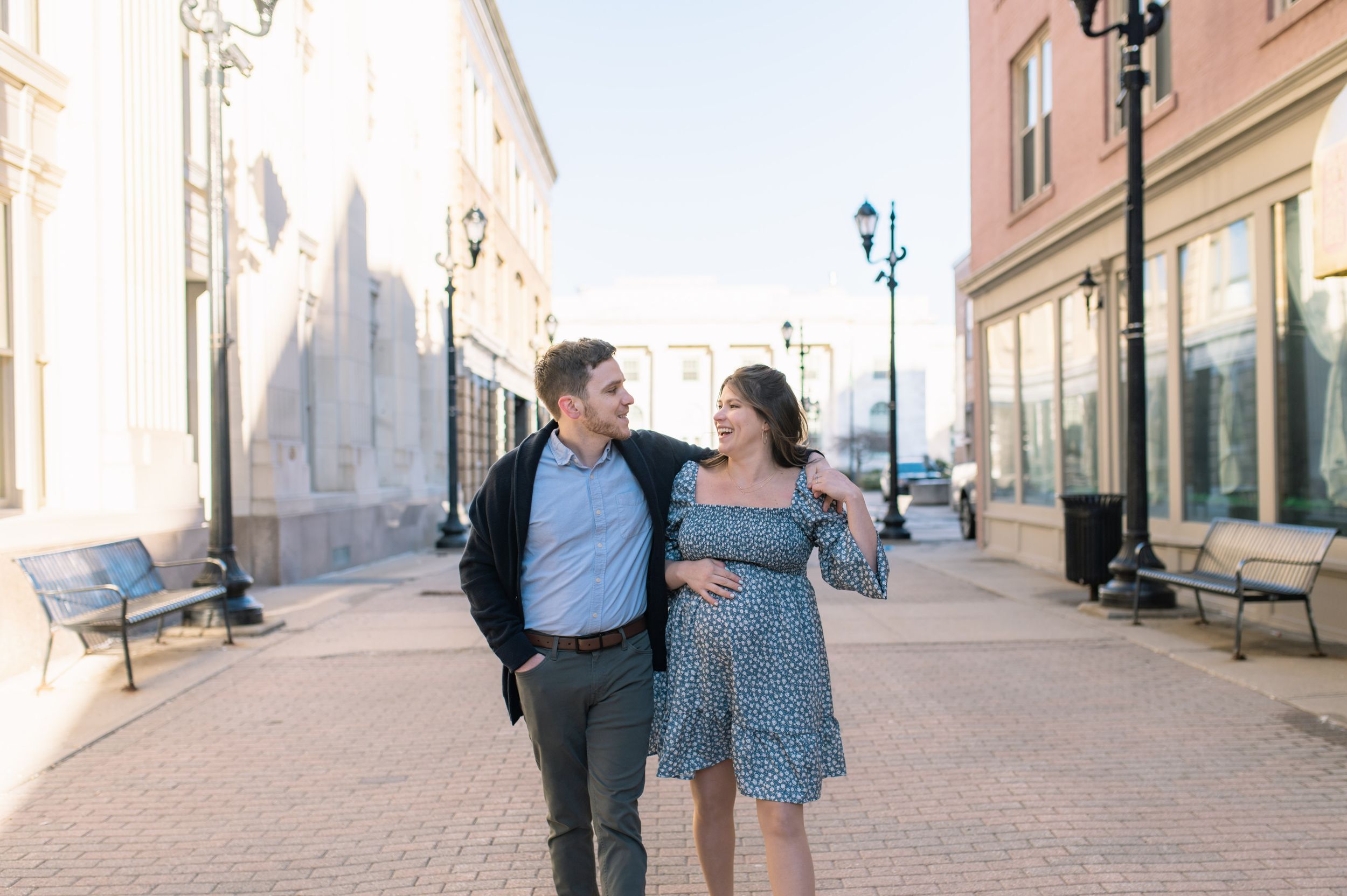 A couple strolls down a charming brick-paved street lined with vintage buildings and lamp posts.
