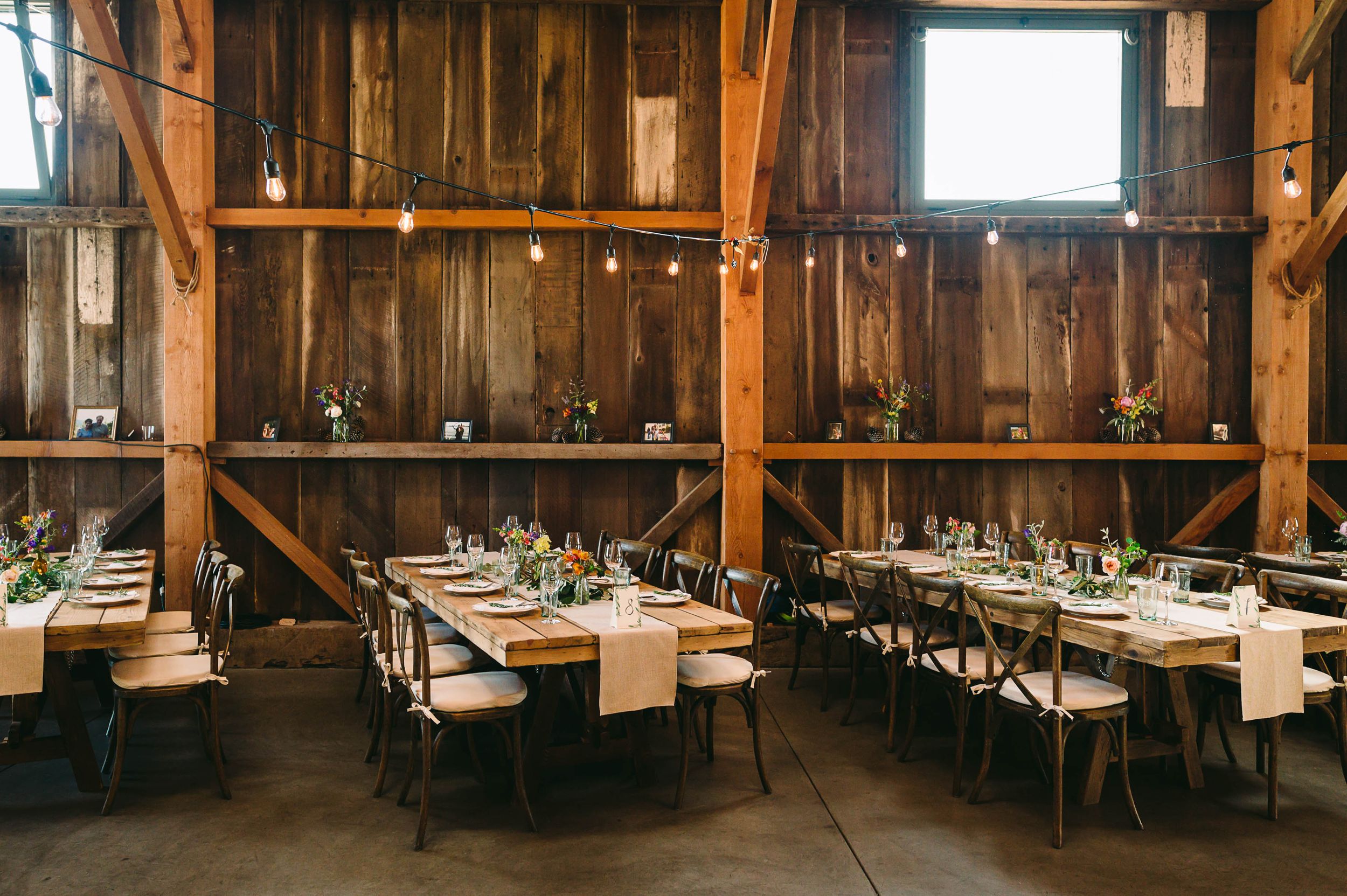 Table and chairs neatly lined up inside the Henry Cowell Hay Barn for a rustic wedding reception with string lights.