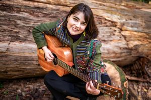 Female in colourful coat playing her guitar outdoors.