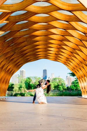 man in suit dipping and kissing woman under Honeycomb at Lincoln Park for engagement pictures in Chicago at sunset