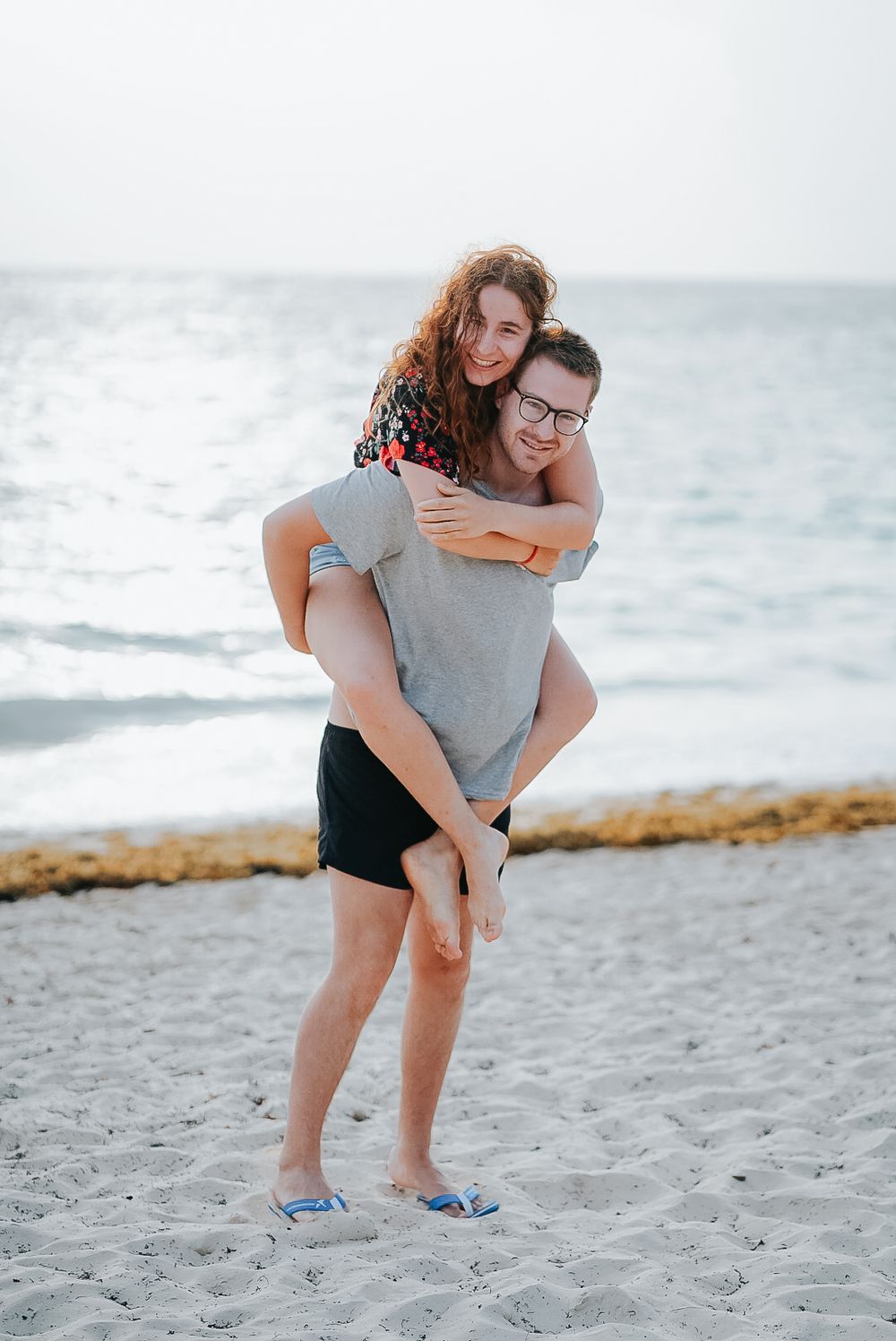 A fun piggyback ride on the beach with ocean waves in the background.