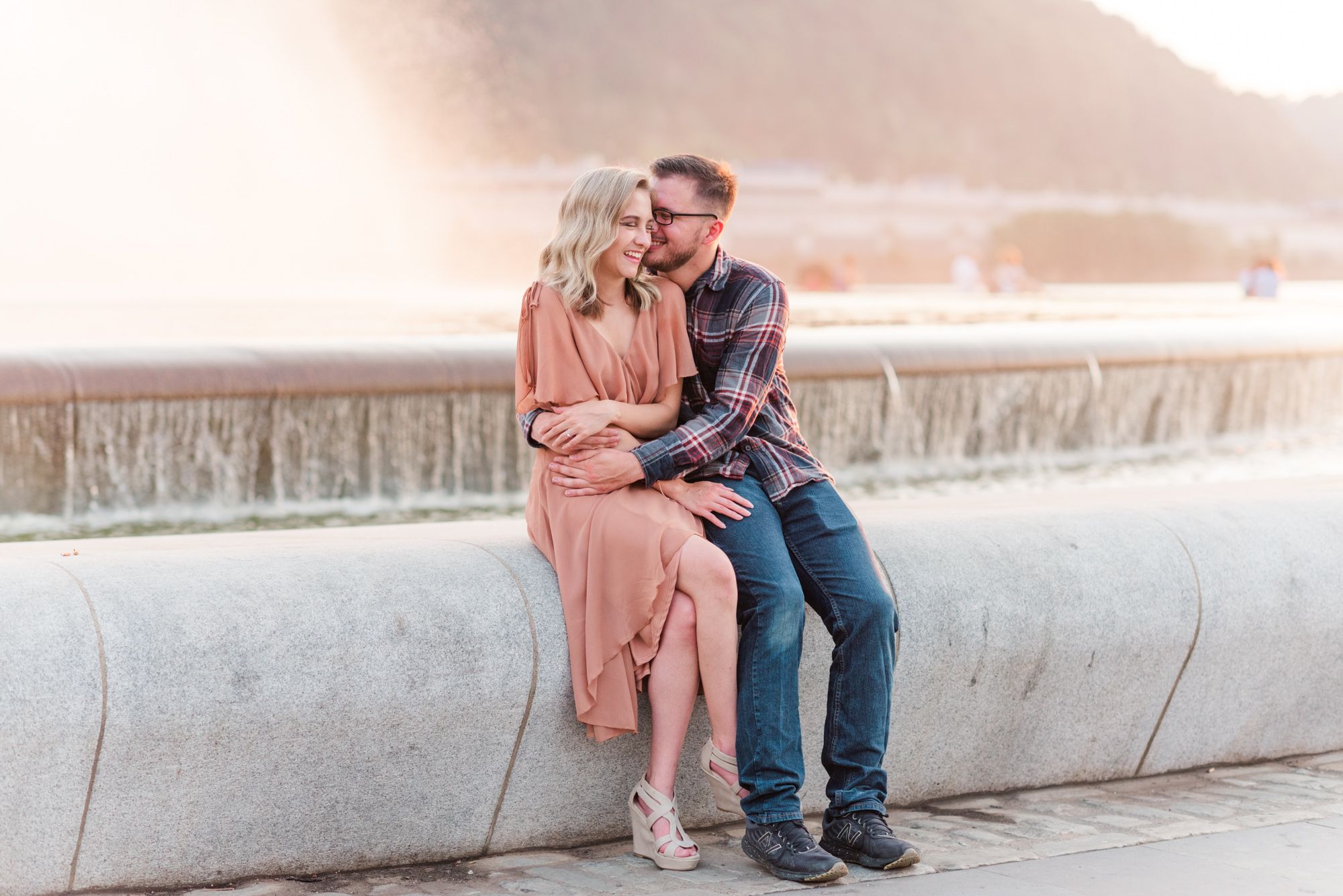 Newly engaged couple sitting in front of fountain at sunset at Point State Park in Pittsburgh, Pennsylvania