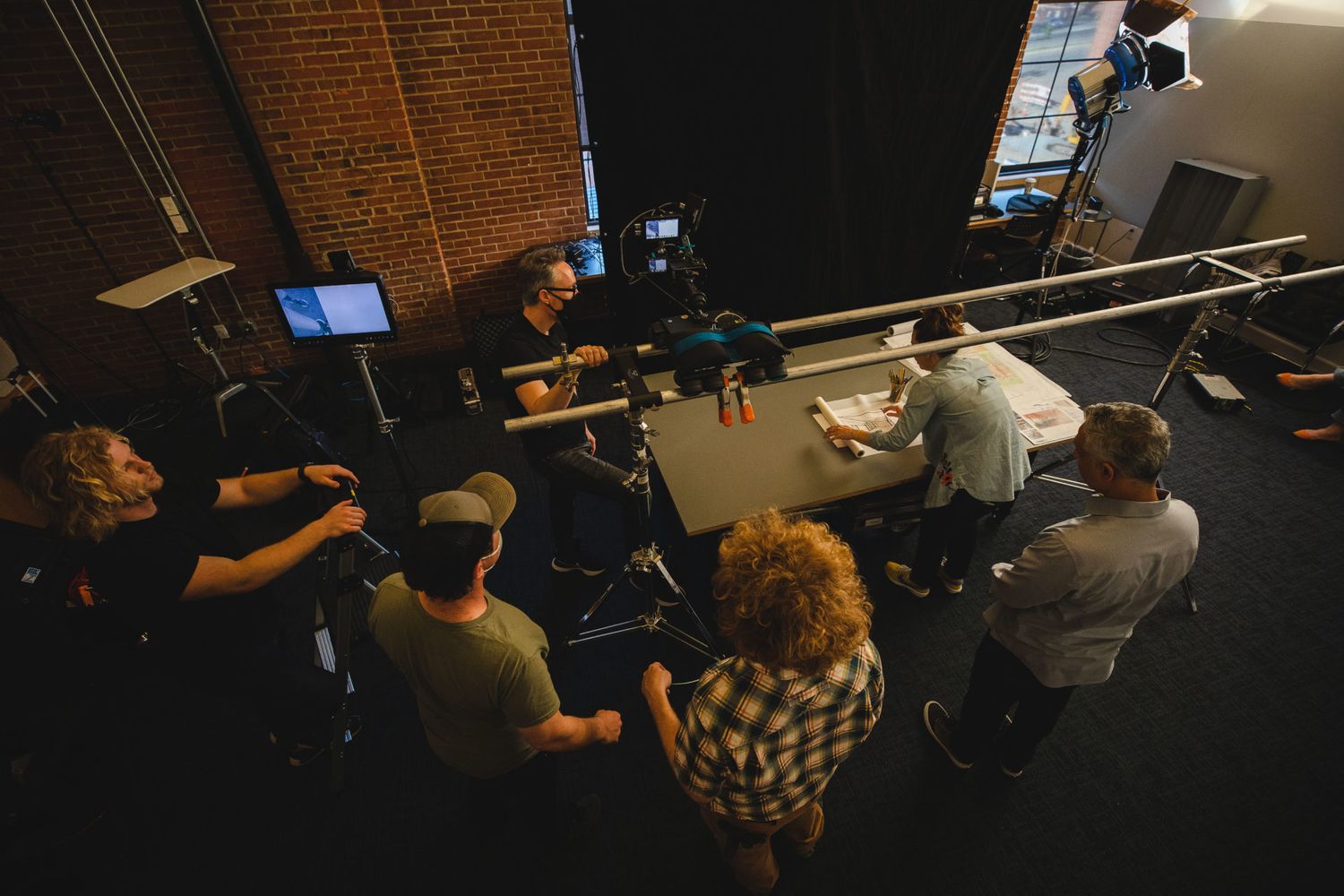 Overhead view of a film production team gathered around equipment in a brick-walled studio.