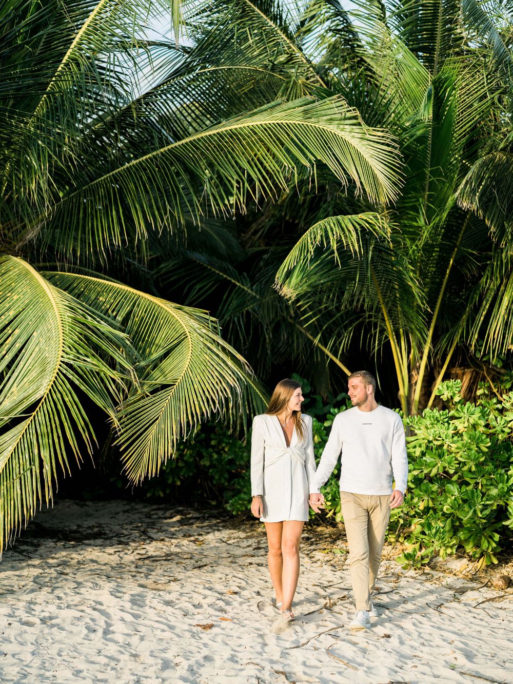 Couple qui marche sur une plage devant des cocotiers