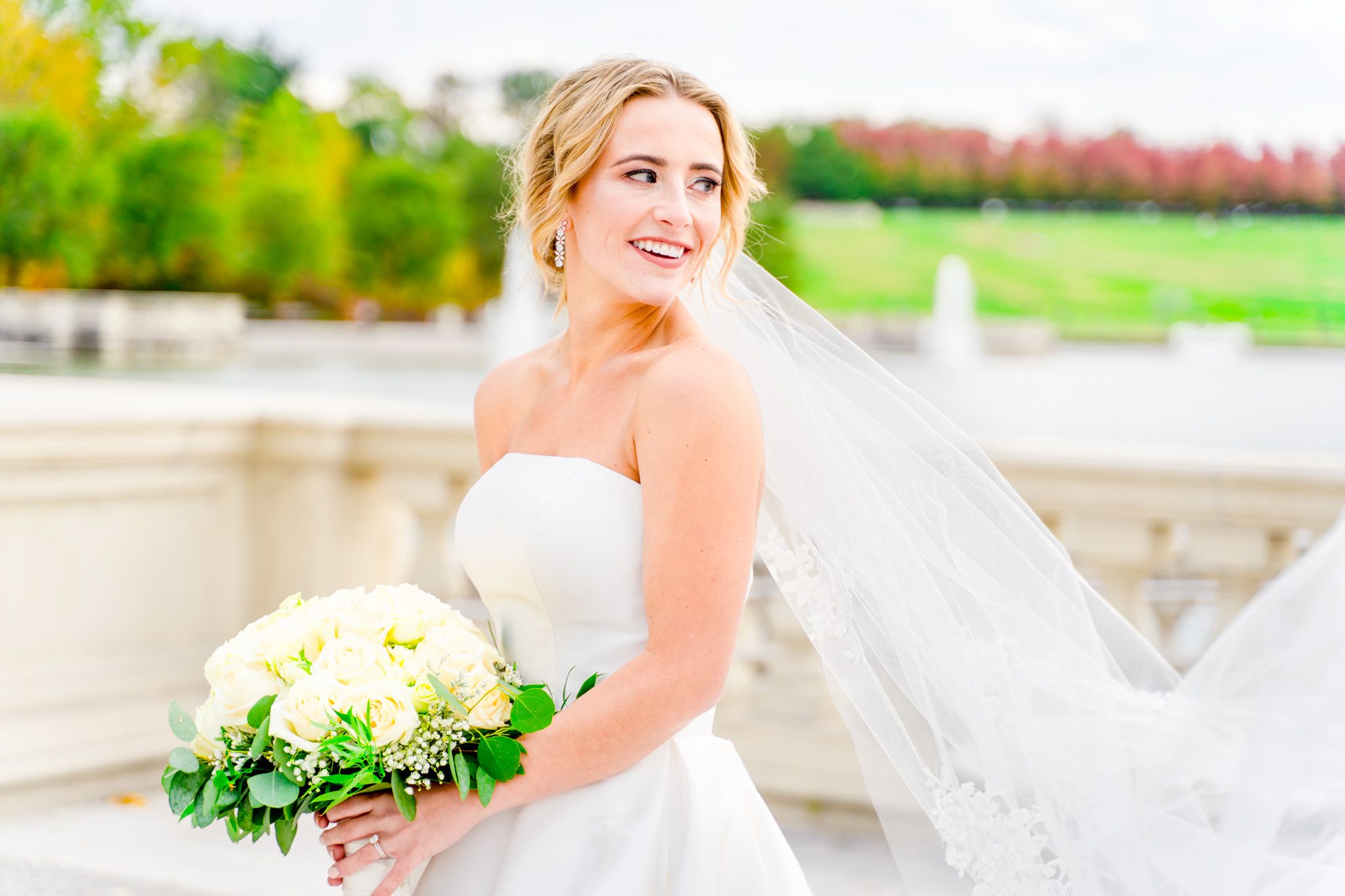 blonde bride with updo and long veil and white bouquet looking over her shoulder in Forest Park wedding pictures