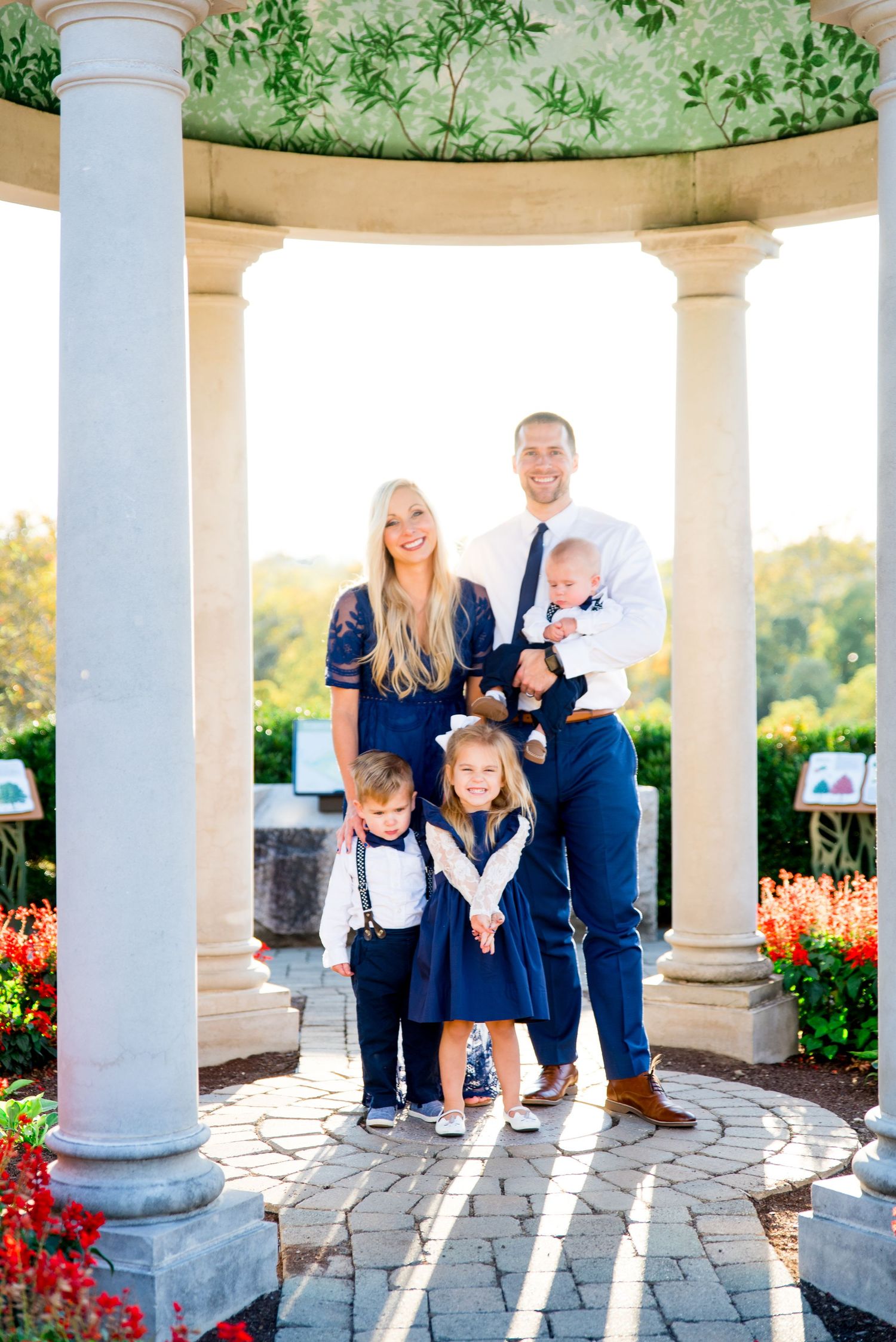 two parents and three young children dresses in white and navy gather in close and smile under a gazebo at sunset