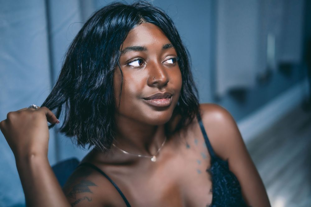 dark skinned woman in a black bralette playing with her hair and looking away