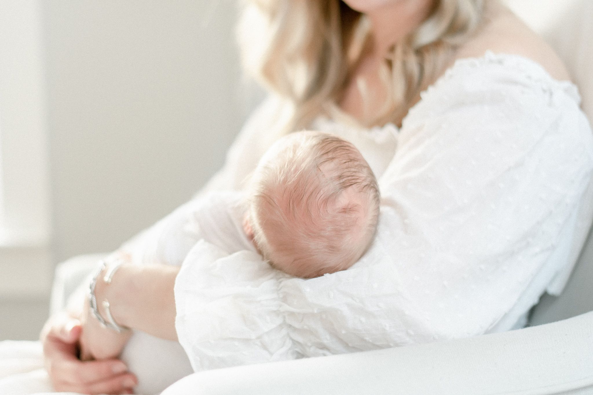 Close up of newborn baby's head, he has blonde hair and his mothers arms are blurry in the background