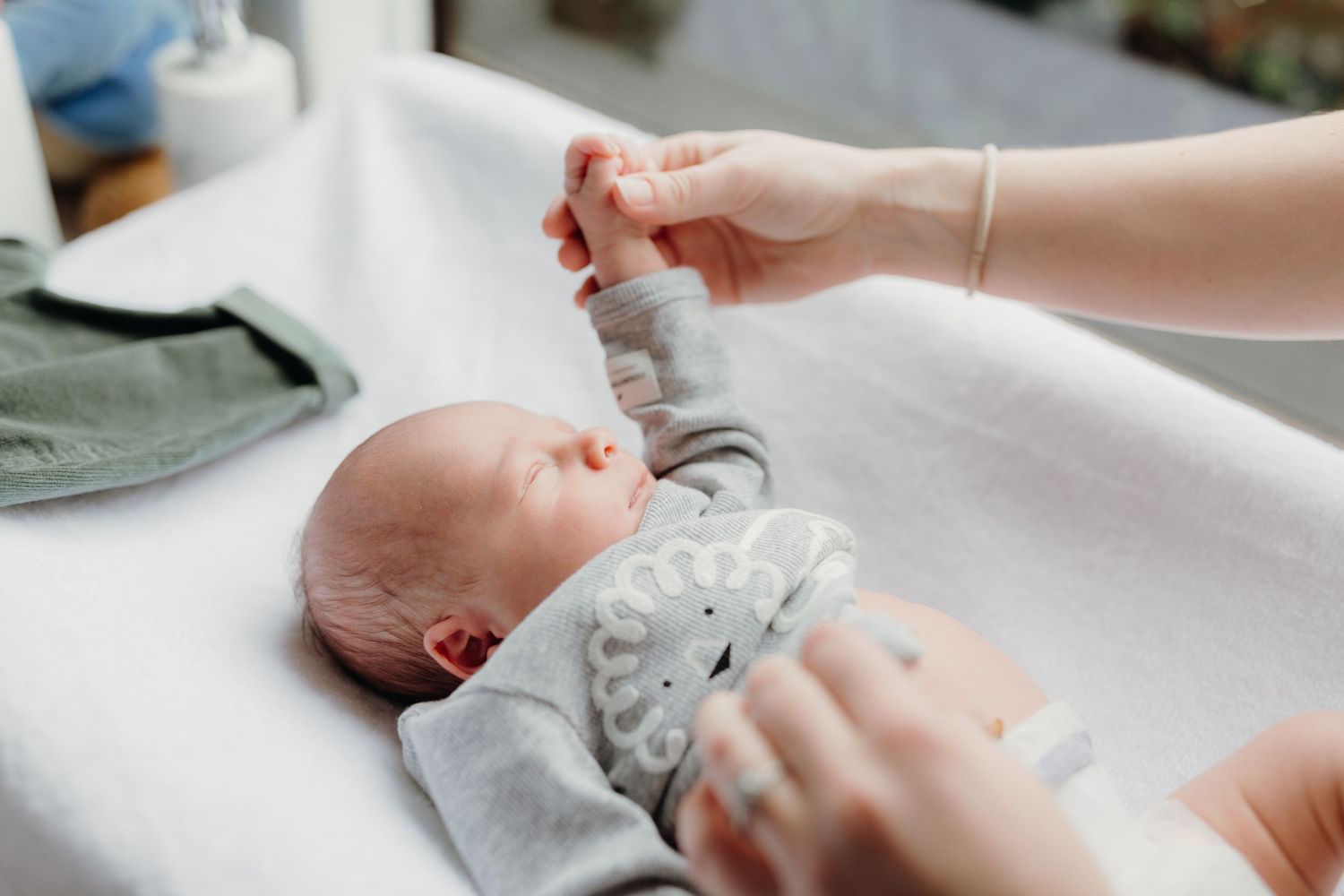 newborn baby being dressed by mother, wearing a grey lion top