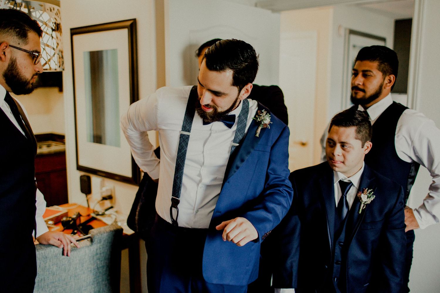 groom putting on blazer jacket with groomsmen watching