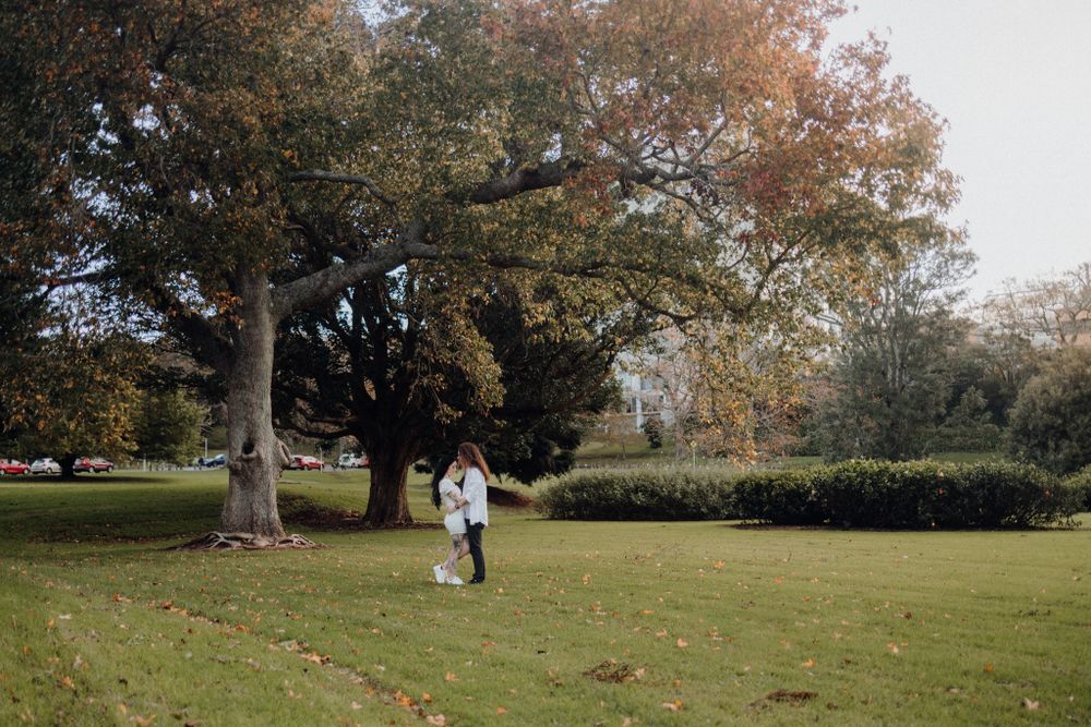 A couple walks together on a grassy lawn surrounded by autumn trees on an overcast day.