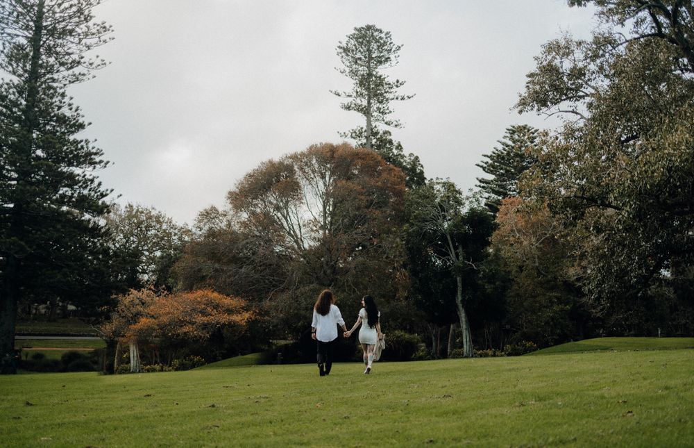 Two people walk hand in hand up a grassy hill surrounded by tall trees.
