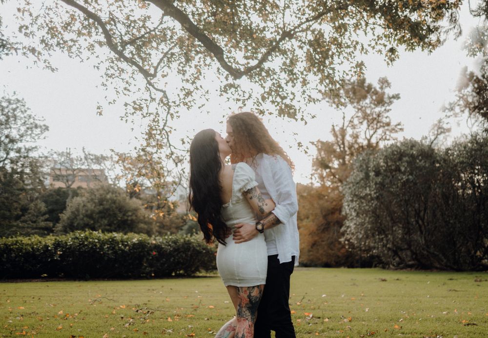 A romantic sunset embrace in a garden setting with trees in the background.
