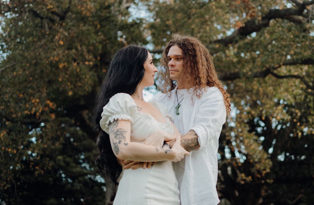 A romantic couple in white outfits share an intimate moment in an autumn park setting.