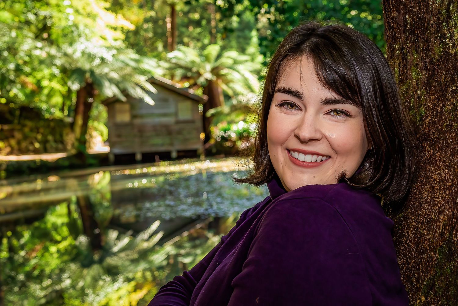 Female in purple jumper with Alfred Nicholas Gardens boathouse behind.