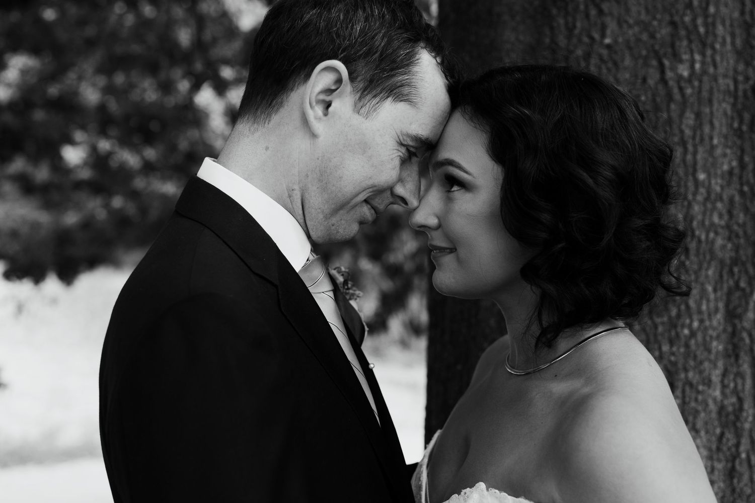 An intimate black and white wedding portrait shows a tender moment between newlyweds.