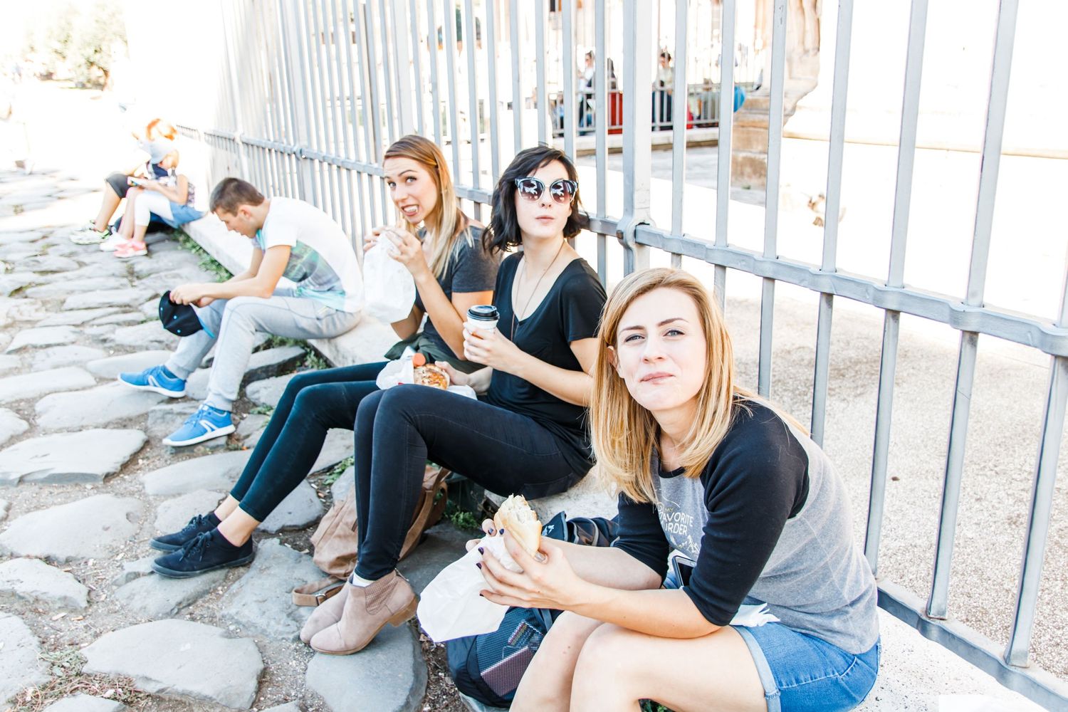 Three women sitting and eating lunch on a cobblestone street in Rome, Italy