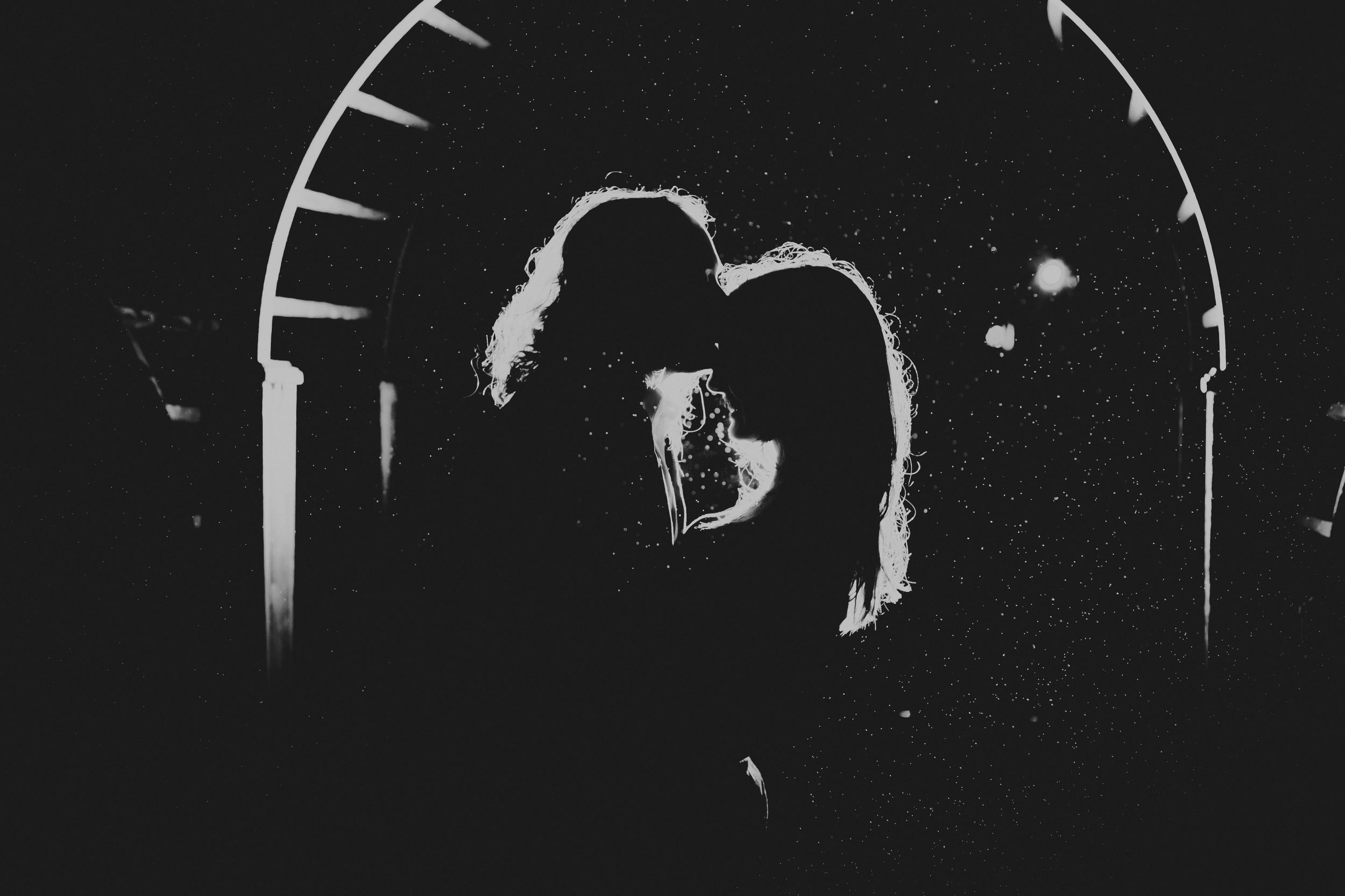 Black and white silhouette photo of a man kissing a woman's forehead in the rain.