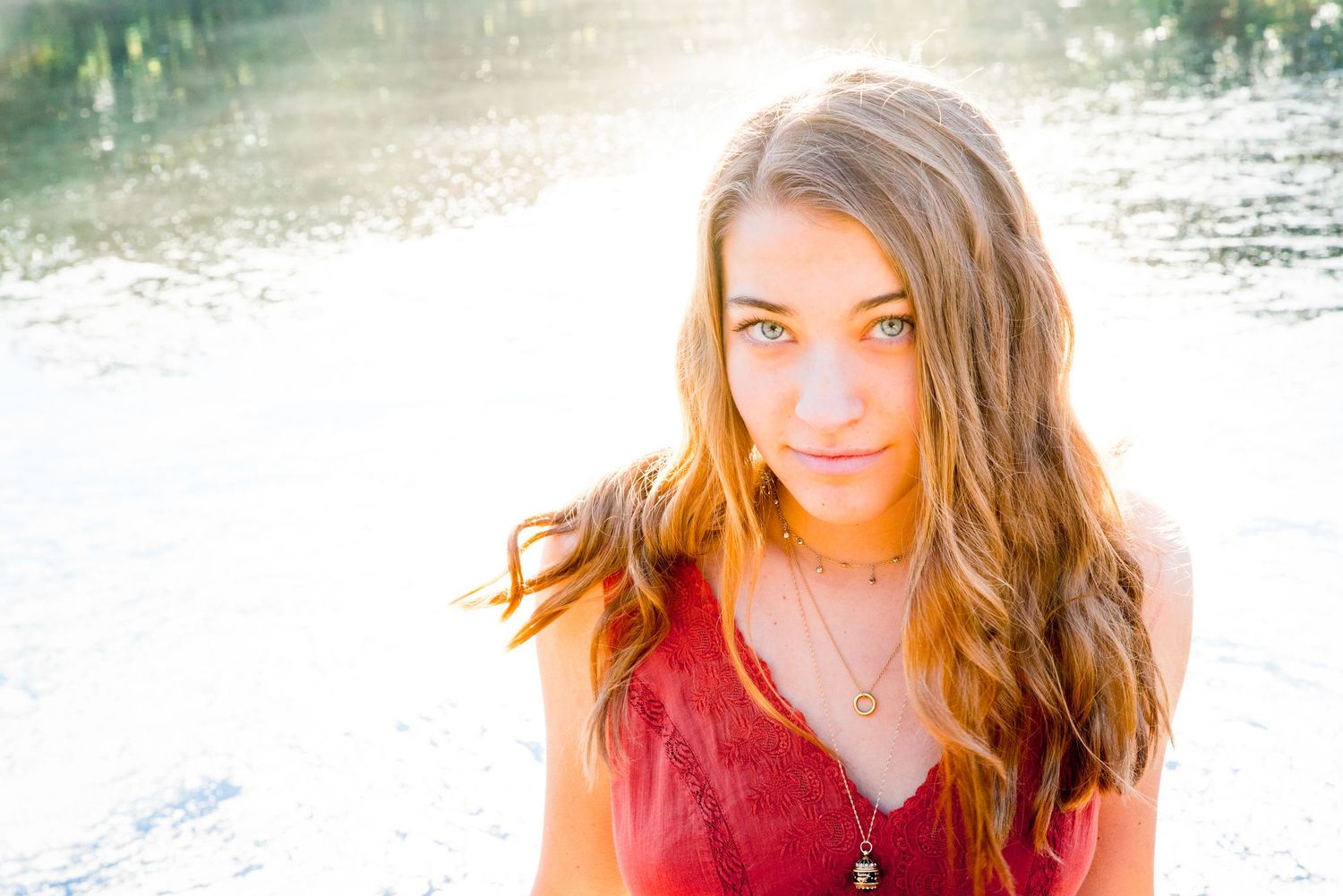 young woman in orange top smirks into the camera and sits in front of a sparkling pond at sunrise in Chicago