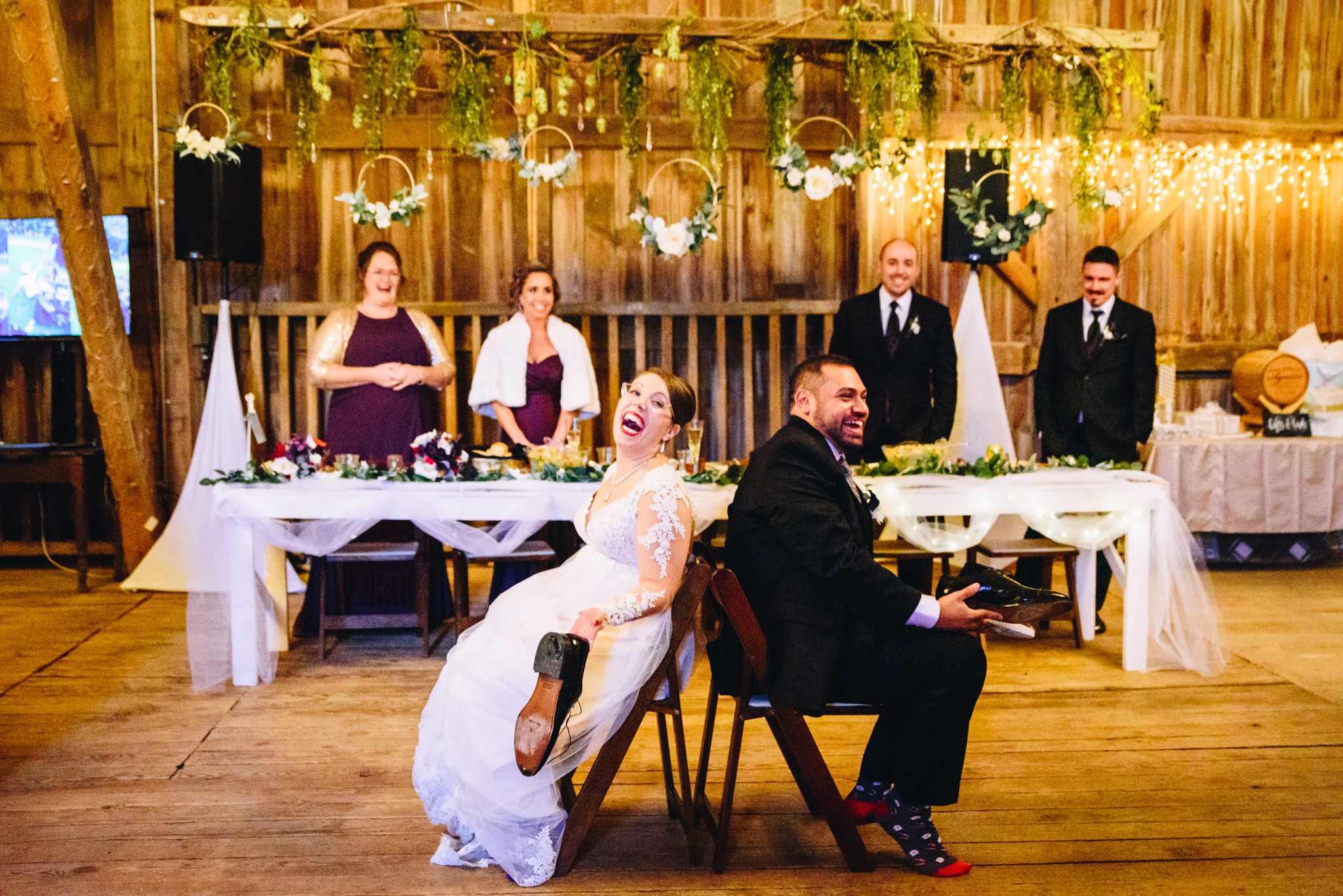 bride and groom sitting back to back laughing holding shoes to play the shoe game at their barn wedding