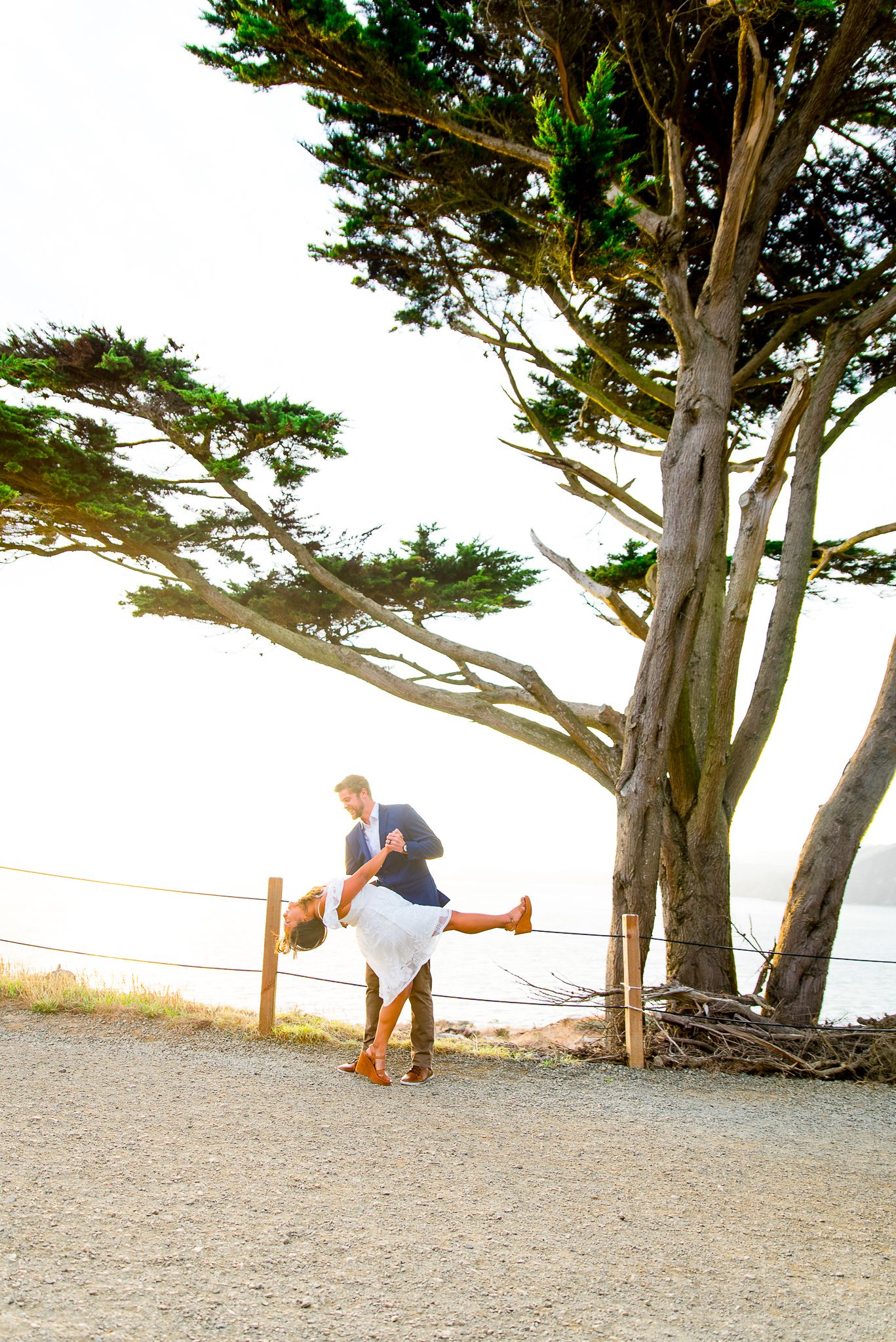 young man dipping his fiance in a white dress at sunset in San Francisco