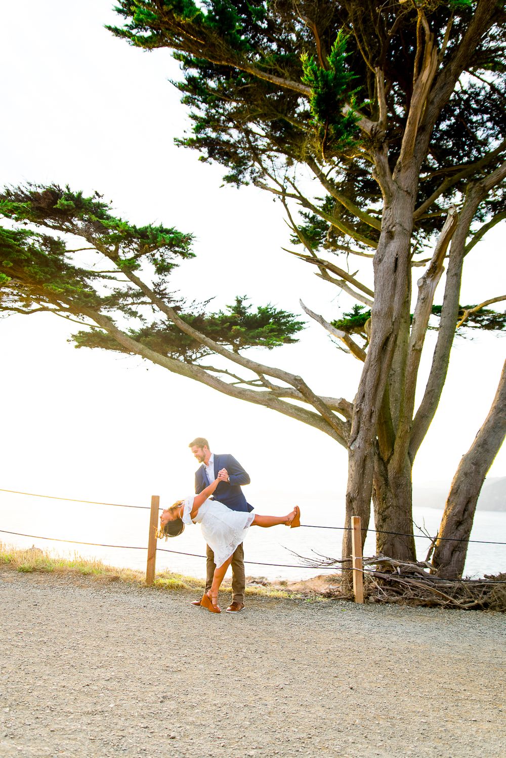 young man dipping his fiance in a white dress at sunset in San Francisco