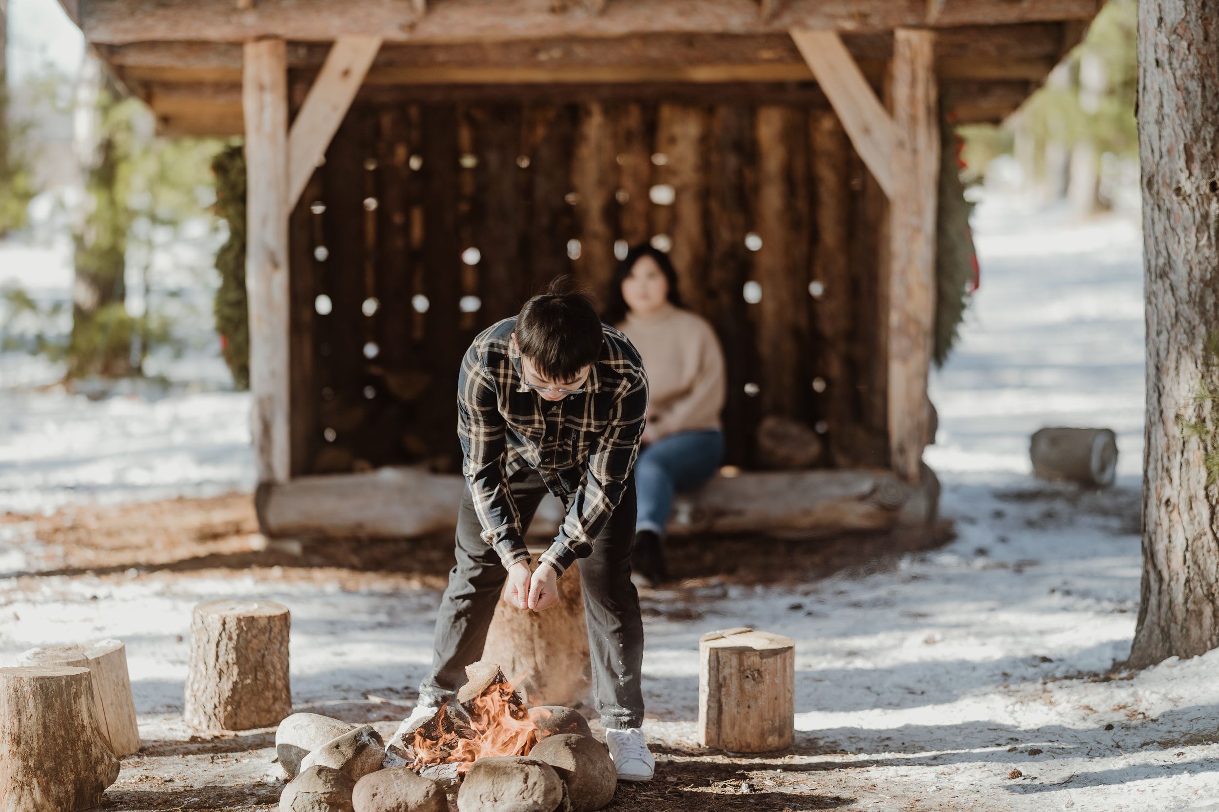 A rustic wooden shelter with logs in the snow and winter decorative lights.