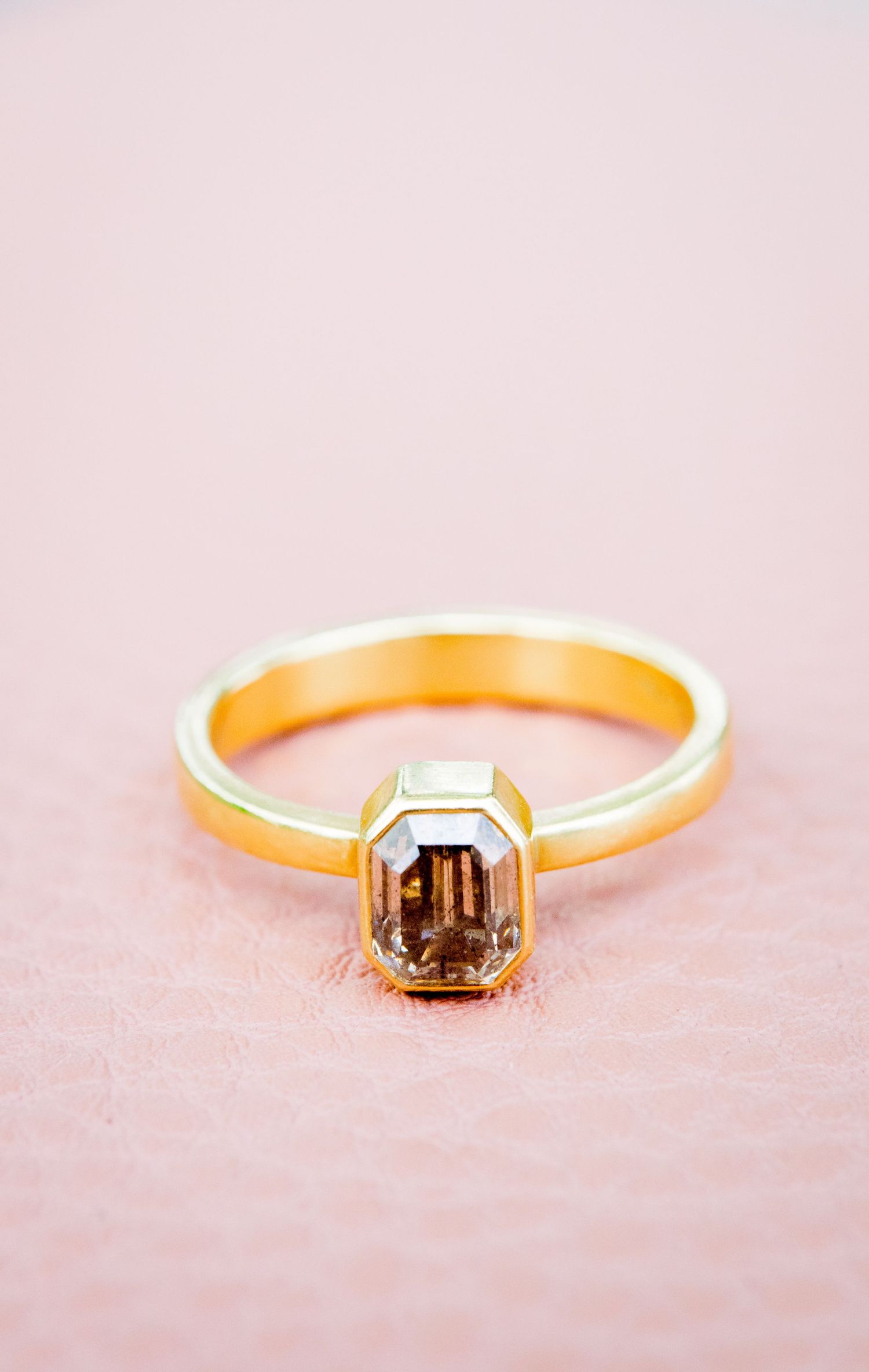 gold emerald cut engagement ring with a smoky natural diamond on a pink leather bag