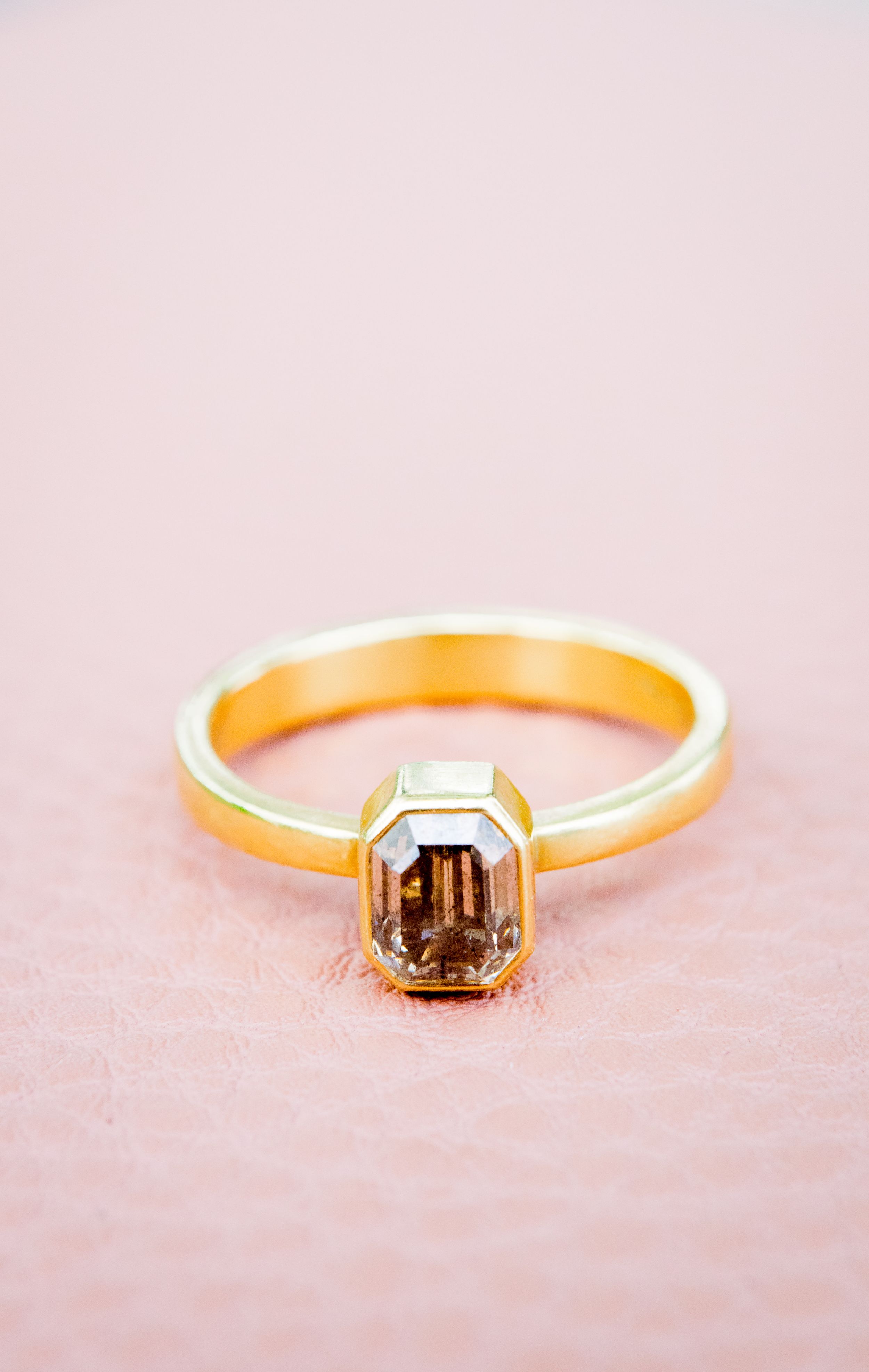 gold emerald cut engagement ring with a smoky natural diamond on a pink leather bag