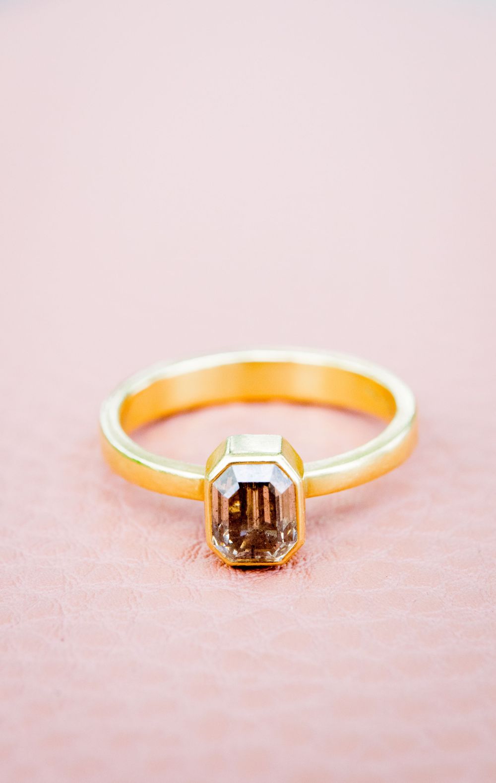 gold emerald cut engagement ring with a smoky natural diamond on a pink leather bag