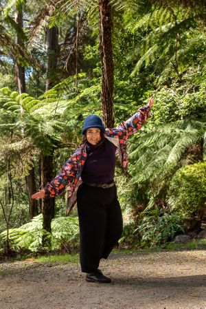Female in colourful coat and blue hat dancing in a garden.