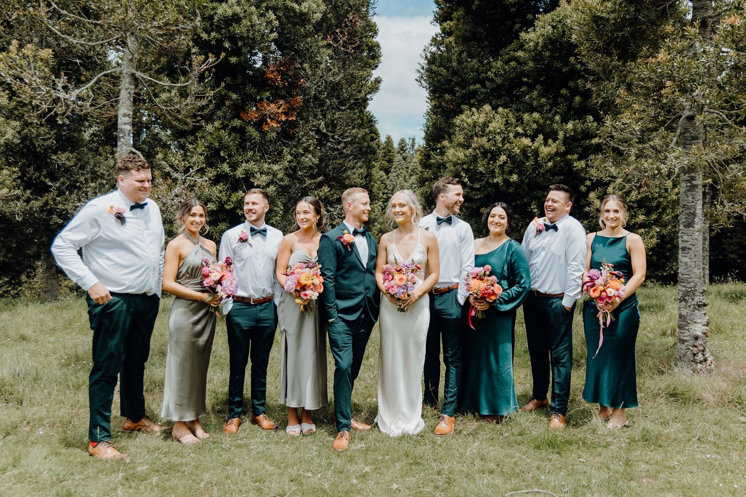 Wedding party members in teal and grey attire pose for formal photo outdoors.